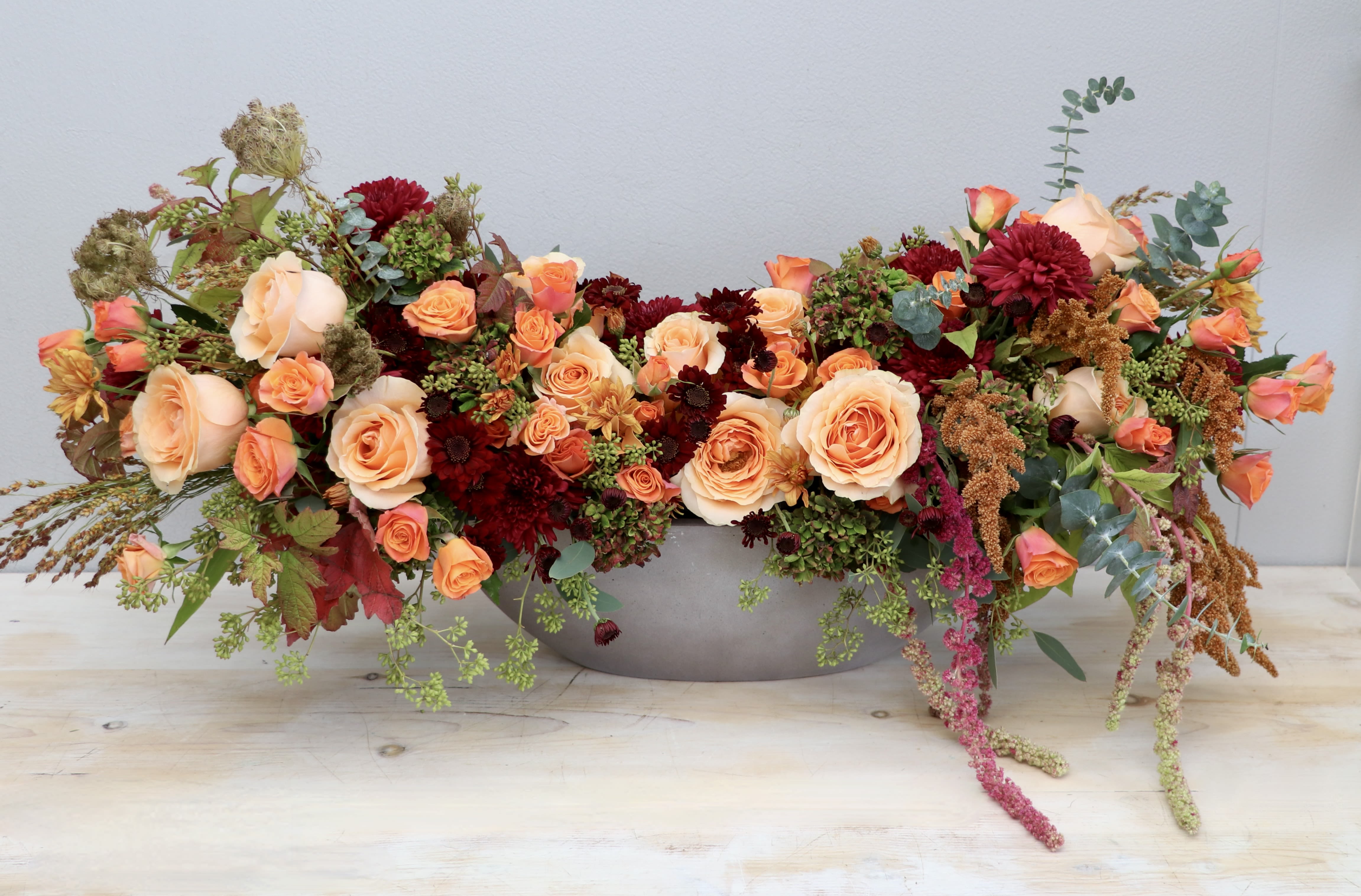 Low oval centerpiece of peach roses and burgundy flowers in a gray bowl-shaped container
