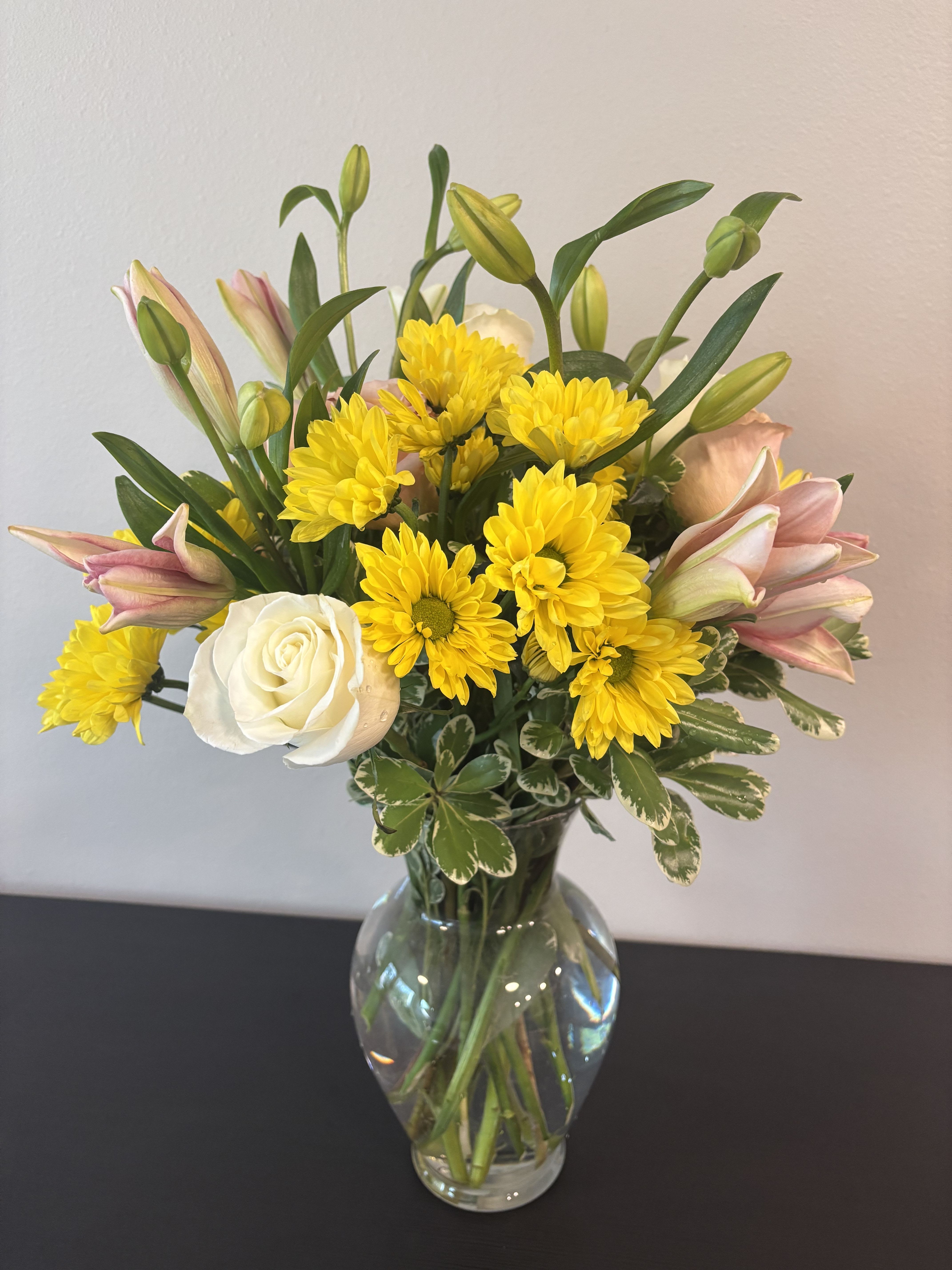 Bouquet of yellow chrysanthemums, pink lilies, and a white rose in a glass vase