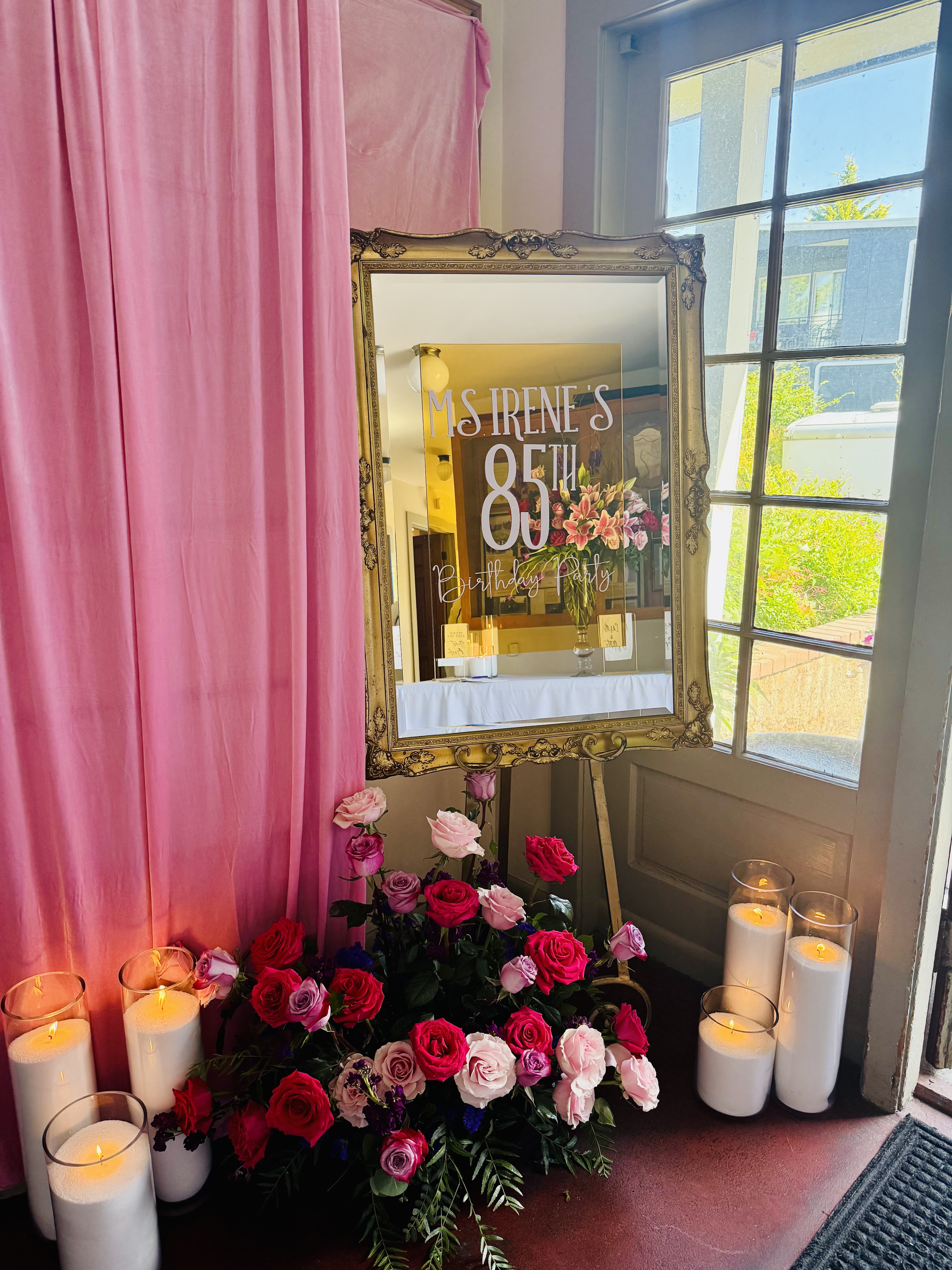 Pink and red rose arrangement with candles beside an ornate mirror sign