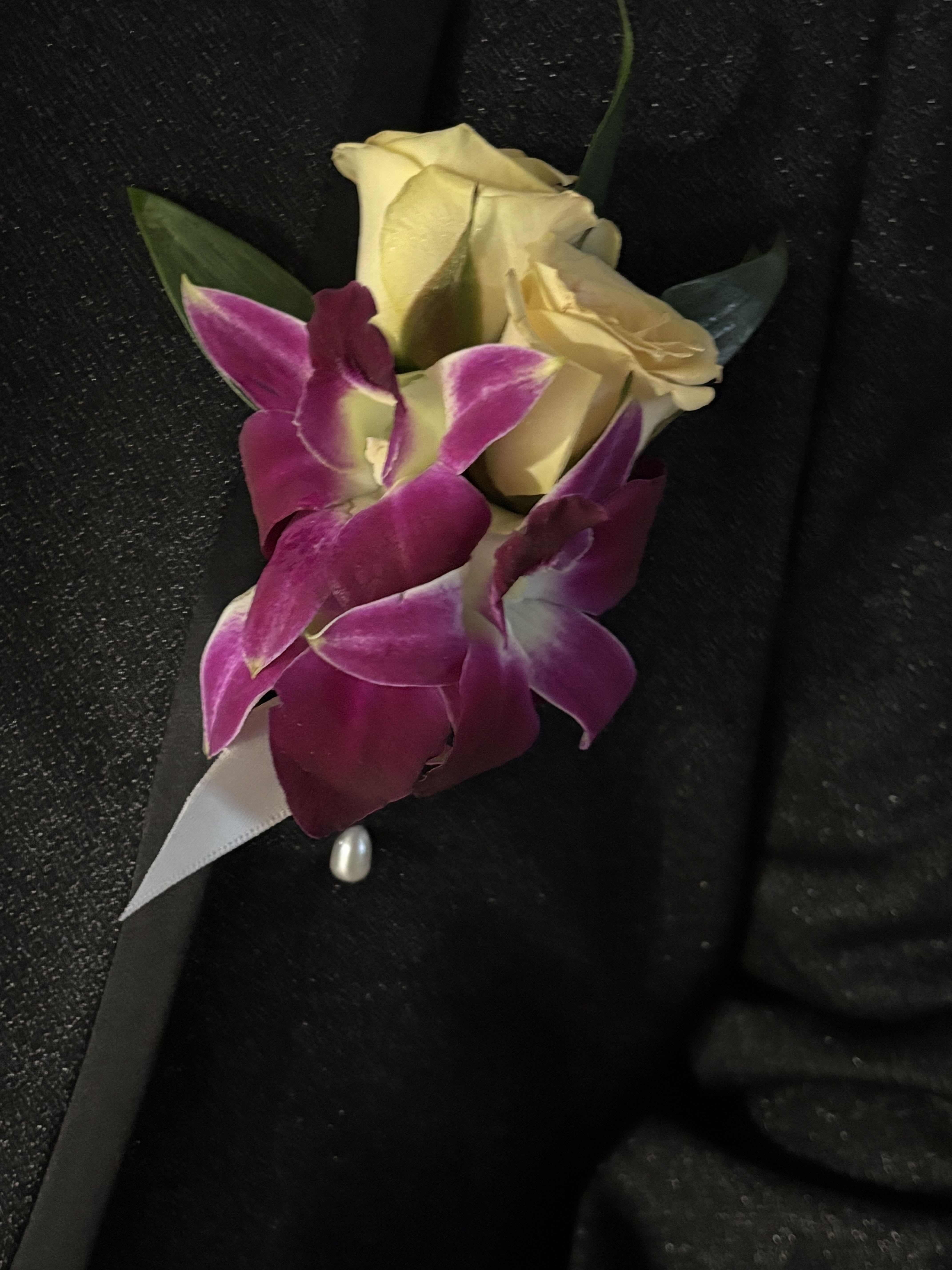 Boutonniere with cream roses and purple orchids on black fabric