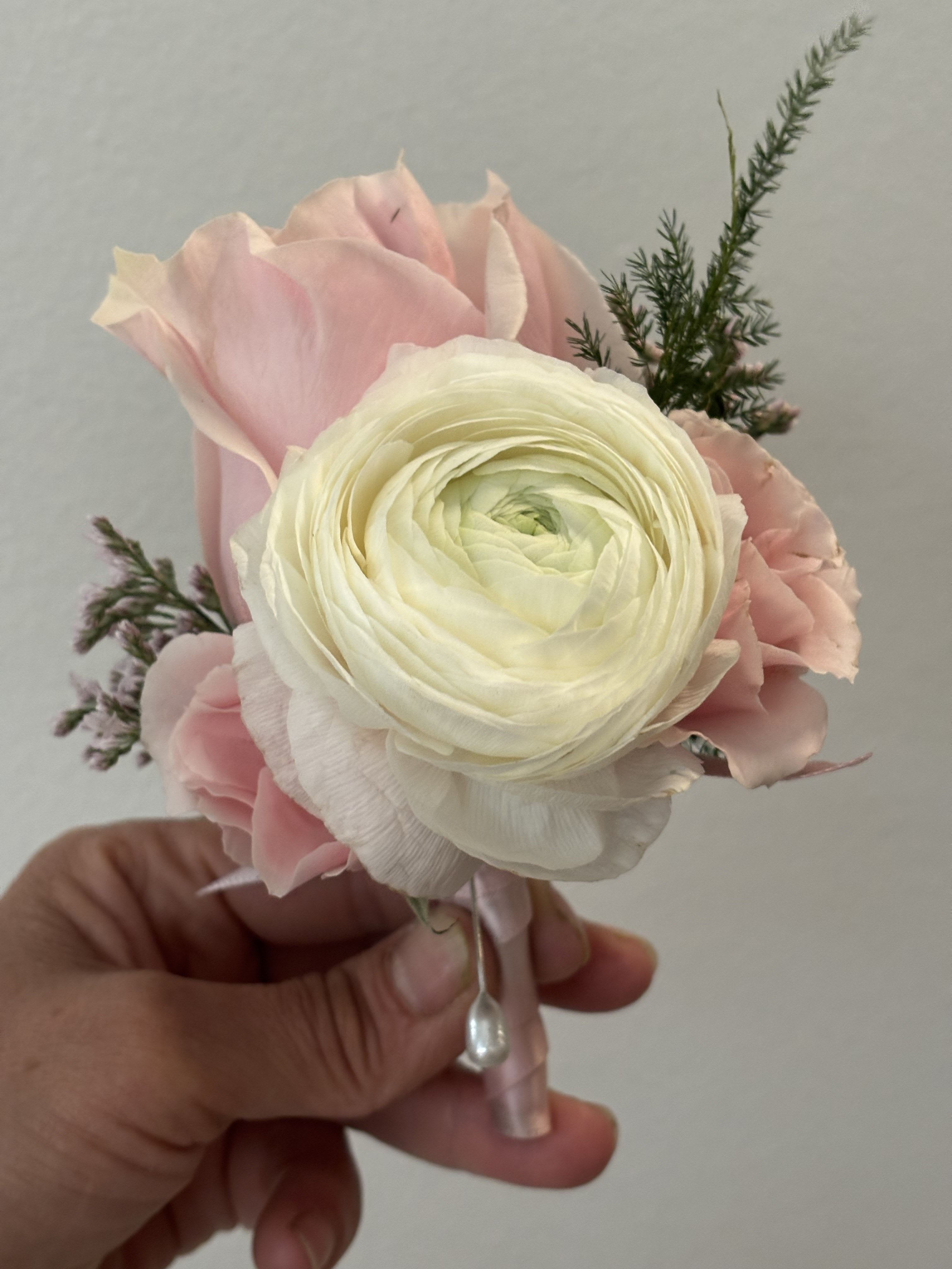 Small pink and white floral boutonniere held in a hand