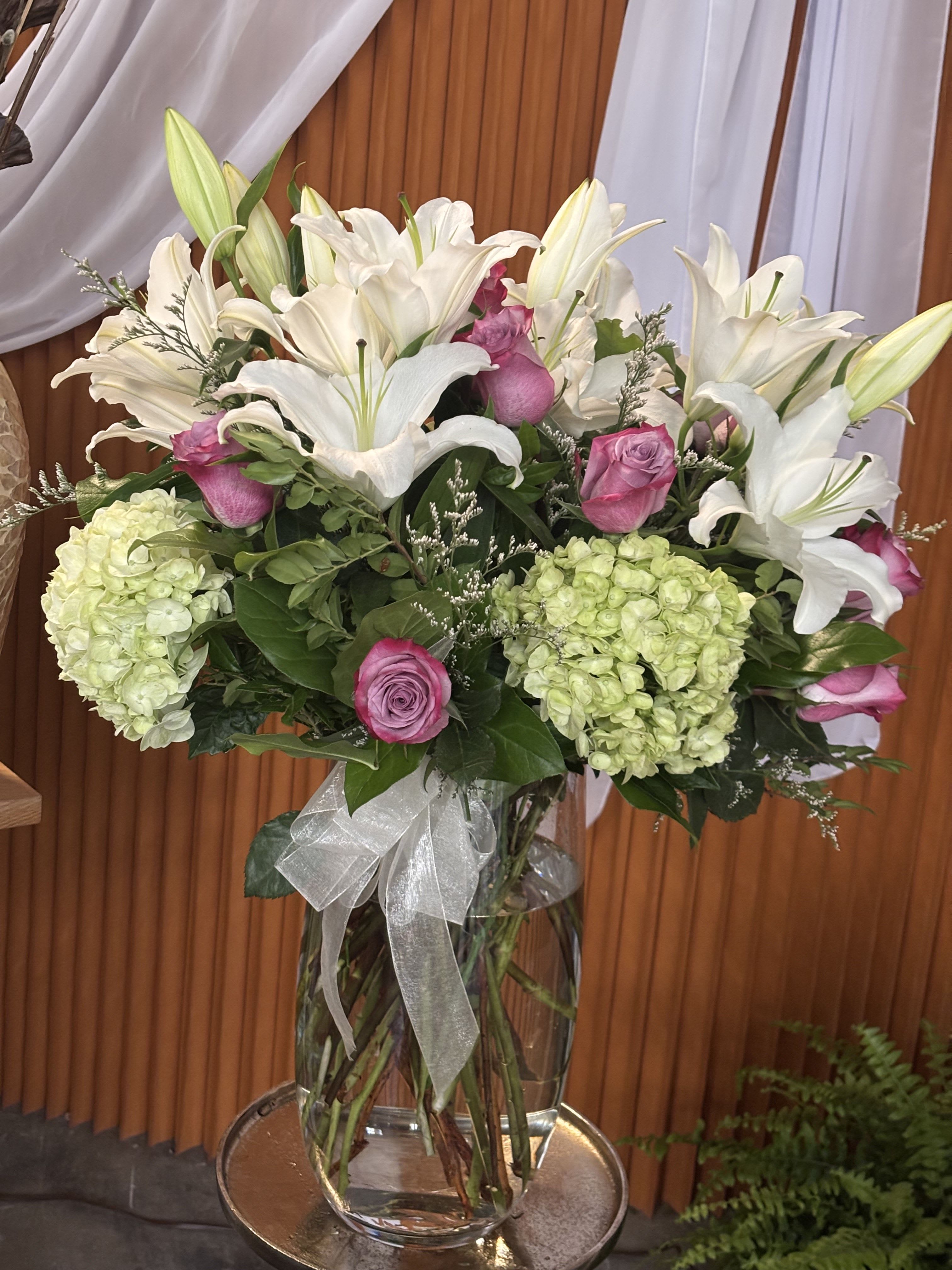 White lilies and pink roses in a glass vase with hydrangeas
