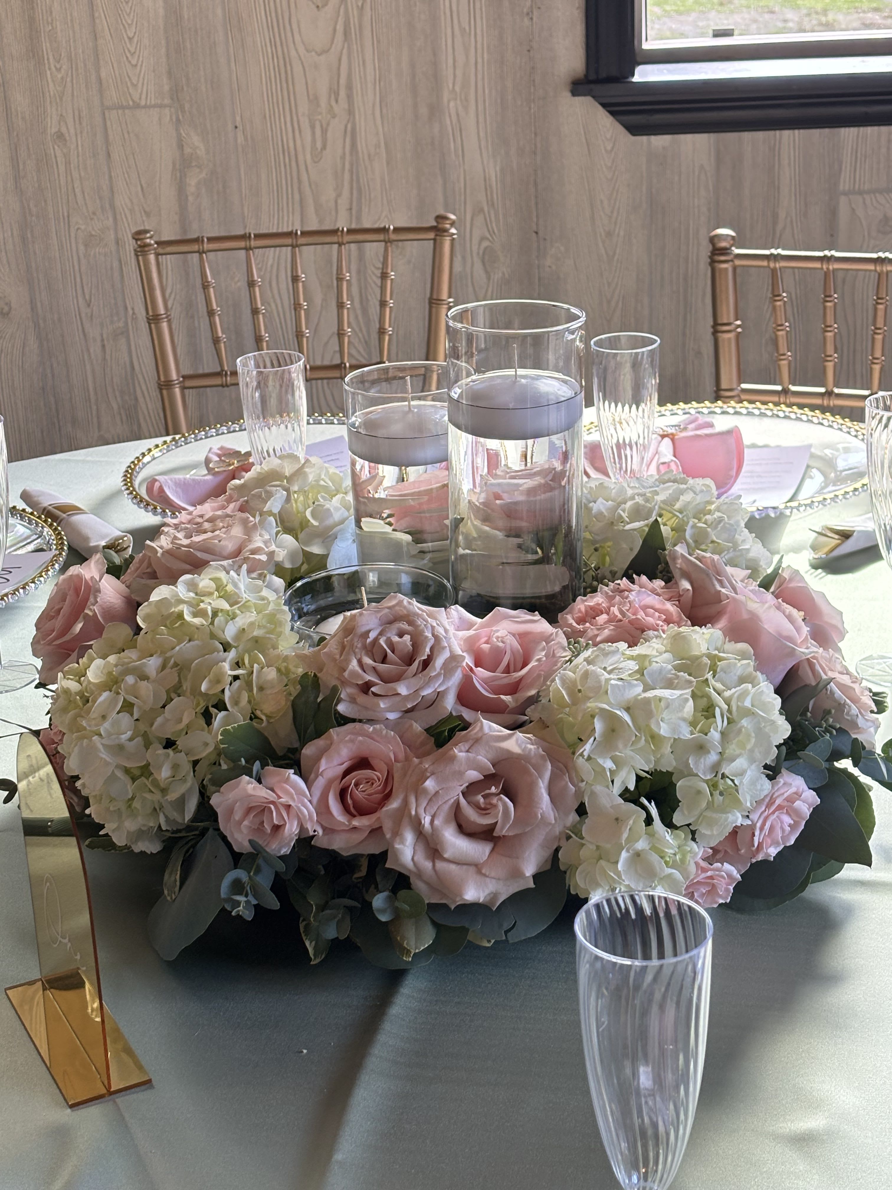 Pink roses and white hydrangeas arranged around glass candle holders on a table