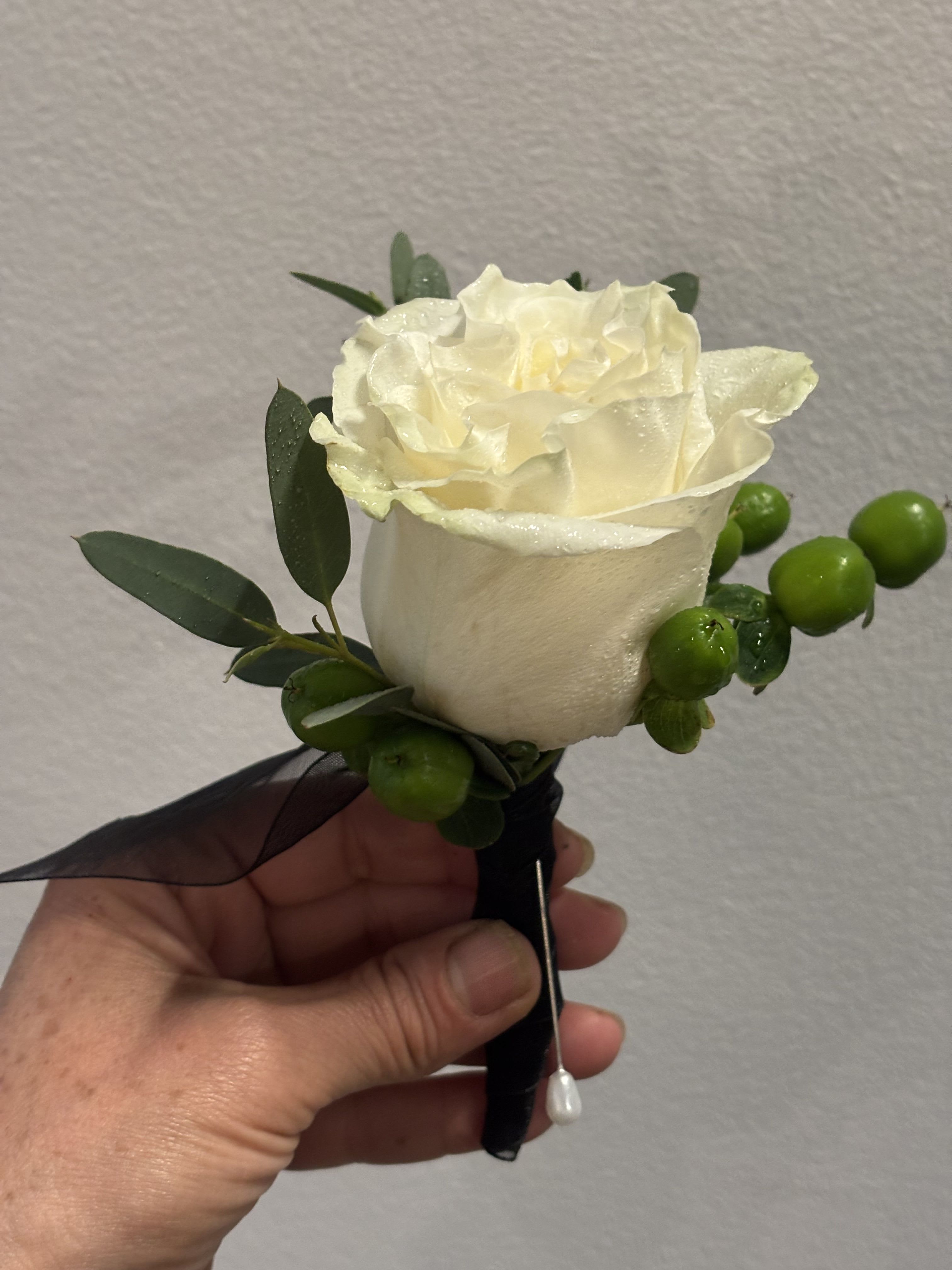 White rose boutonniere with green berries and dark ribbon