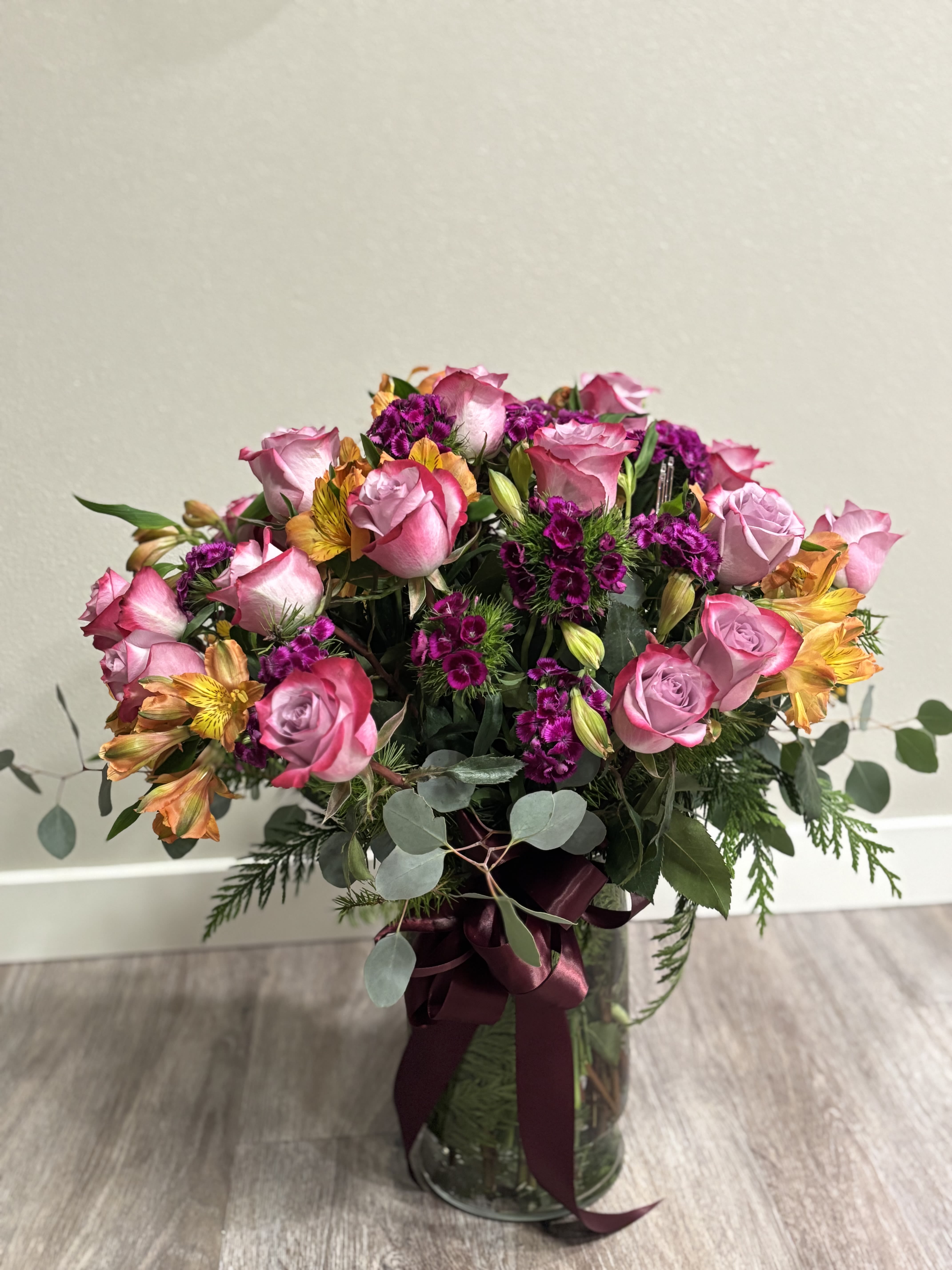 Pink roses and purple flowers in a glass vase with a burgundy ribbon