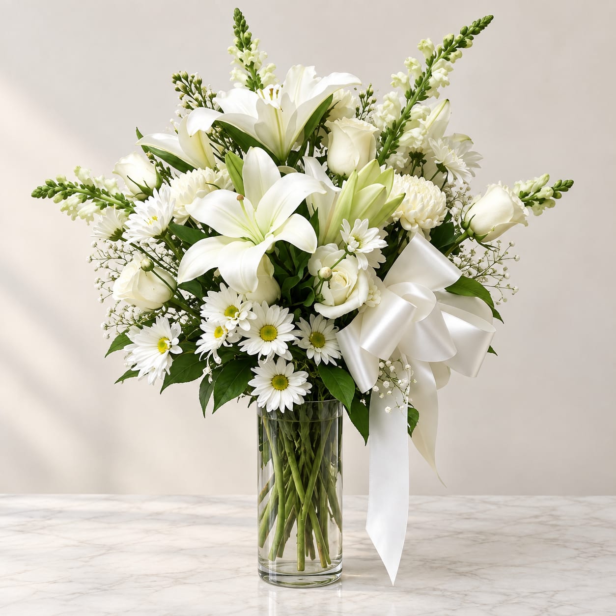 White lilies and daisies arranged in a clear glass vase with a white ribbon