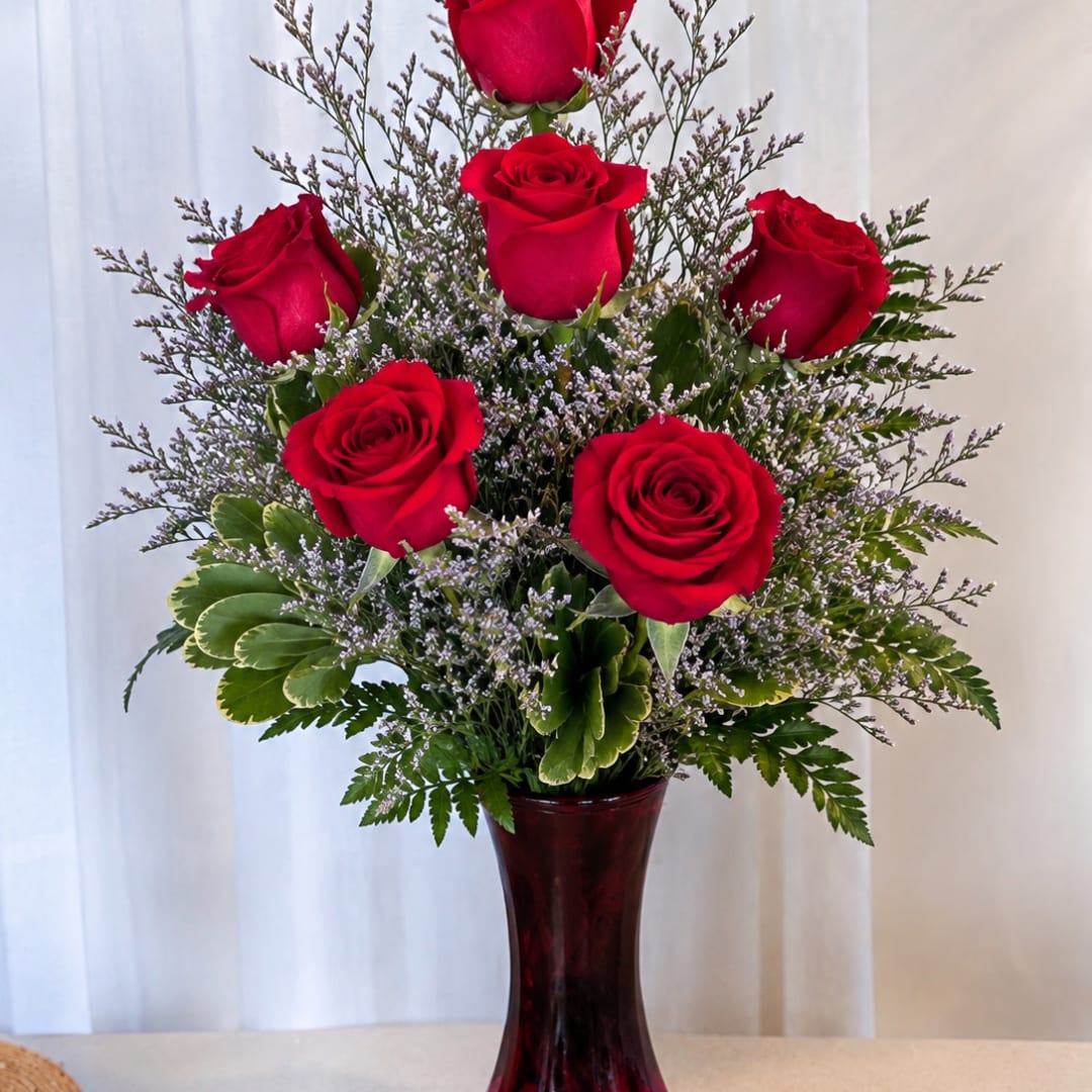Red roses arranged in a tall vase with greenery