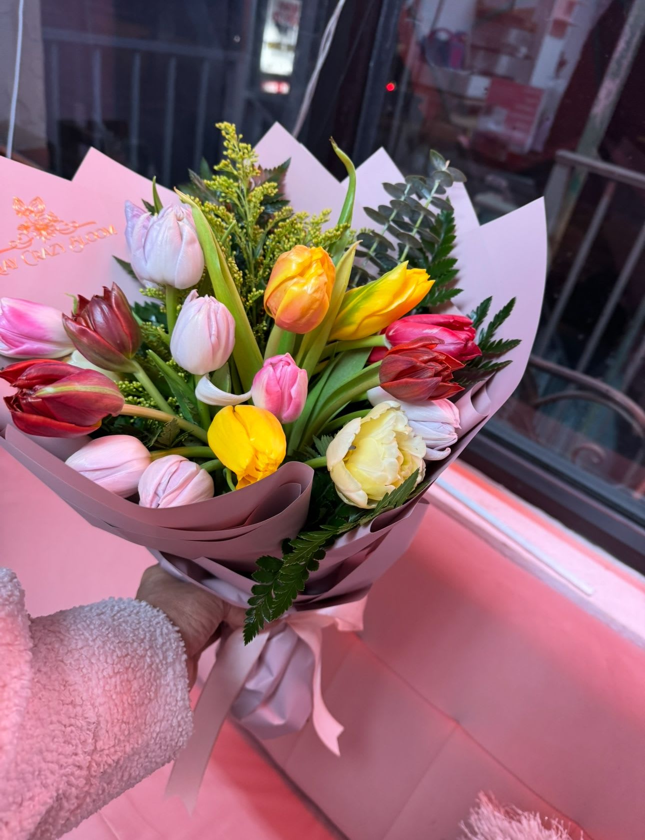 Handheld bouquet of multicolored tulips wrapped in pink paper