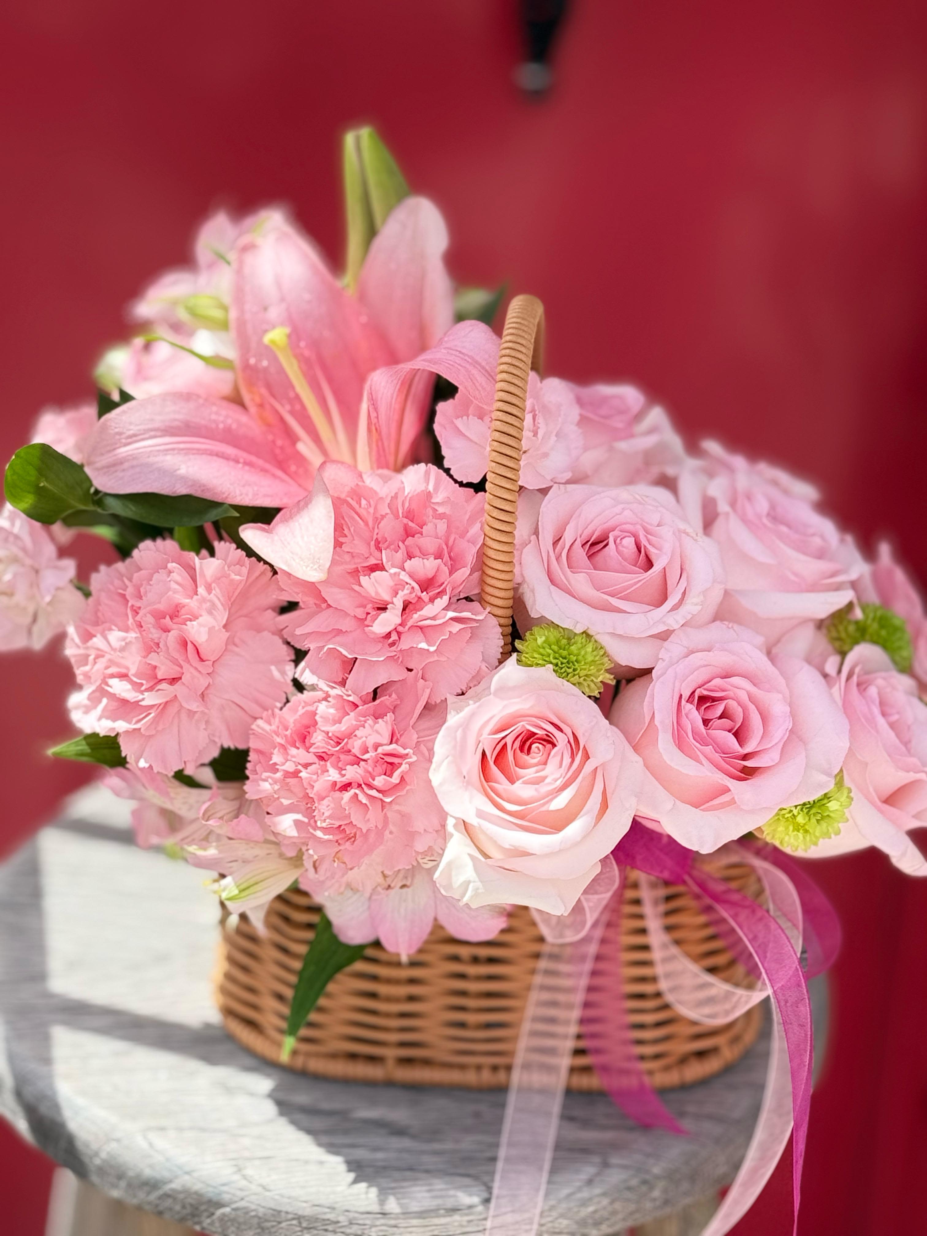 Pink roses and carnations in a wicker basket with ribbon