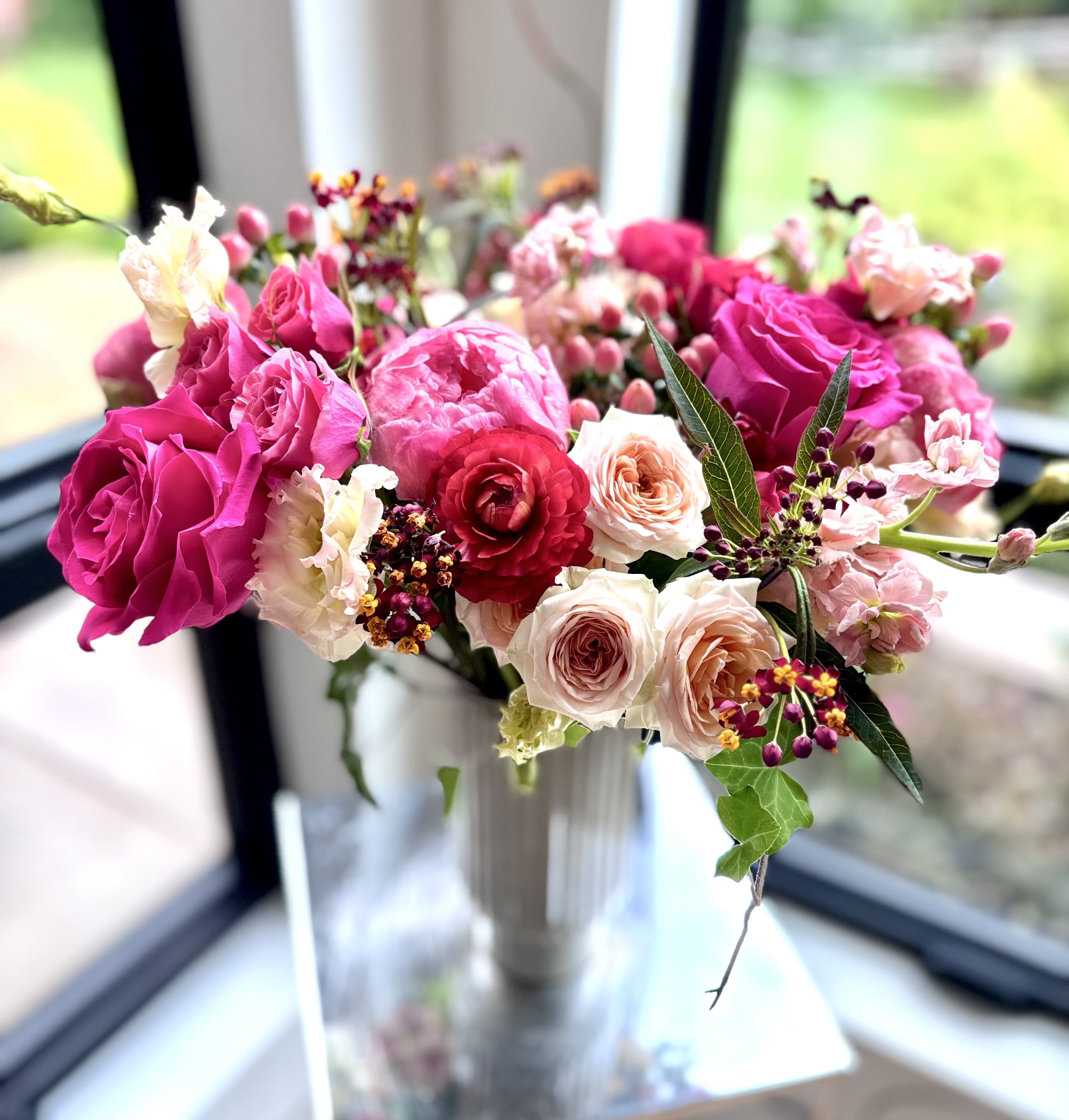 Jardin de Rose - A romantic garden-style arrangement with layered textures and organic movement, it blends bold pink and red tones with peachy pastels for a luxurious yet whimsical feel. Fresh greenery and berry accents add depth and elegance, creating a centerpiece that feels both modern and timeless.
