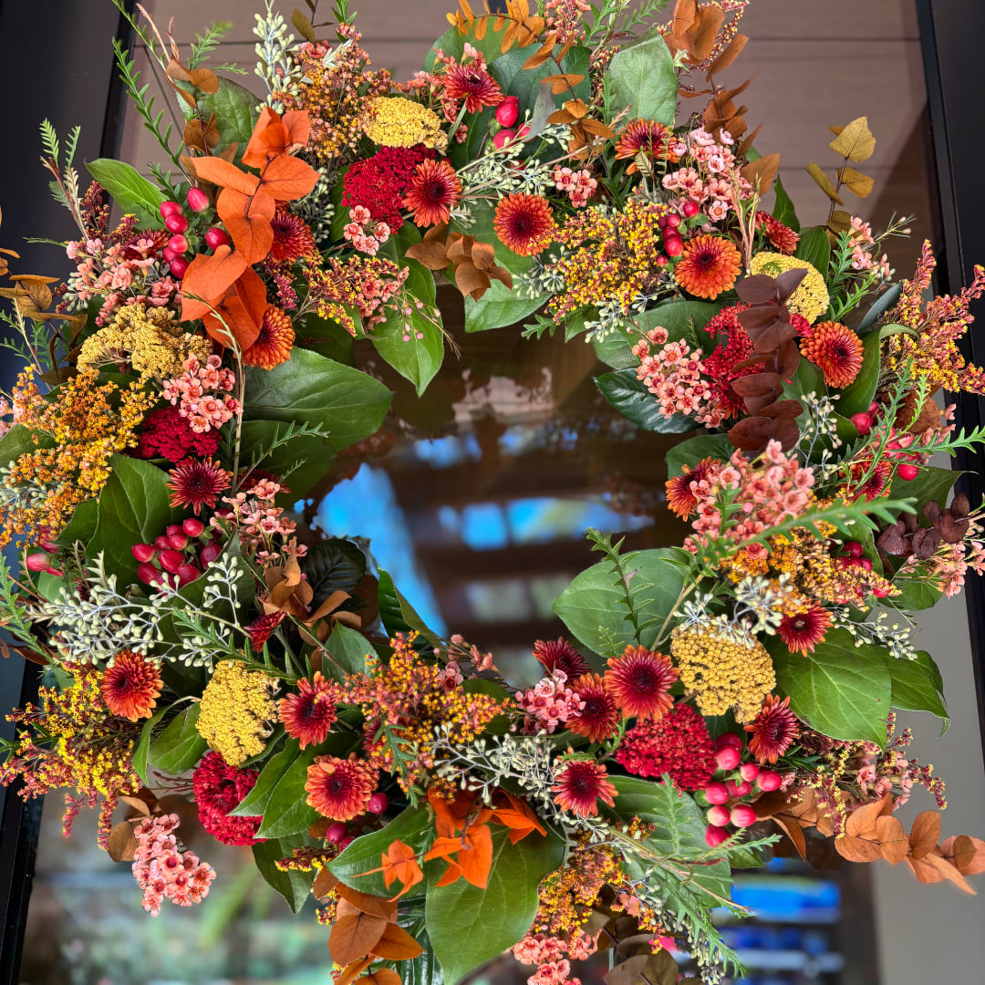 Autumn wreath with orange, red, and yellow flowers on a dark door