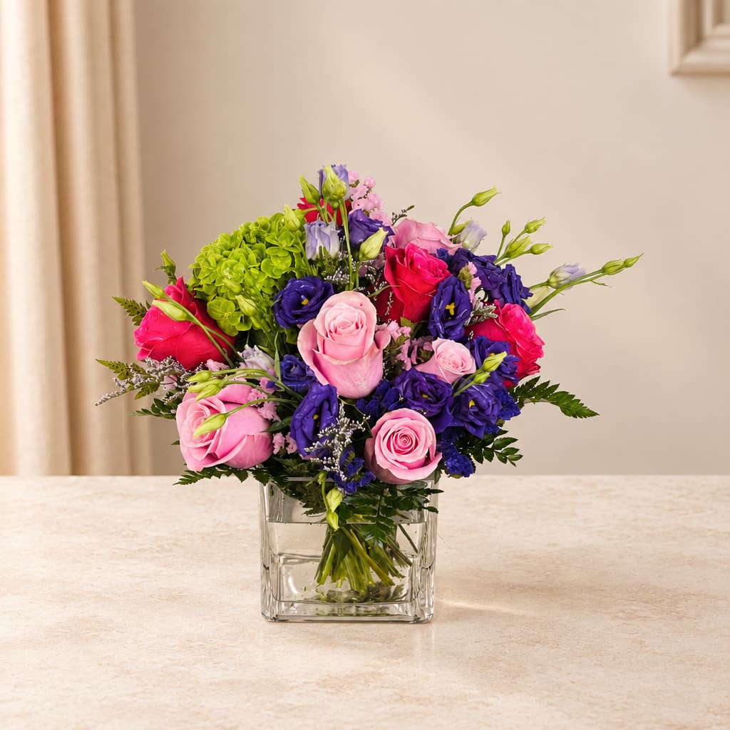 Bouquet of pink, purple, and red roses in a clear square vase