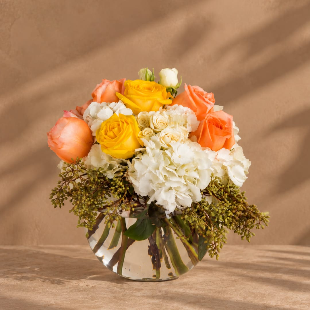 Bouquet of yellow, peach, and white flowers in a clear glass vase