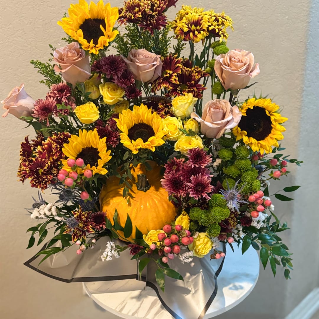 Autumn floral arrangement with sunflowers, roses, and chrysanthemums around a pumpkin