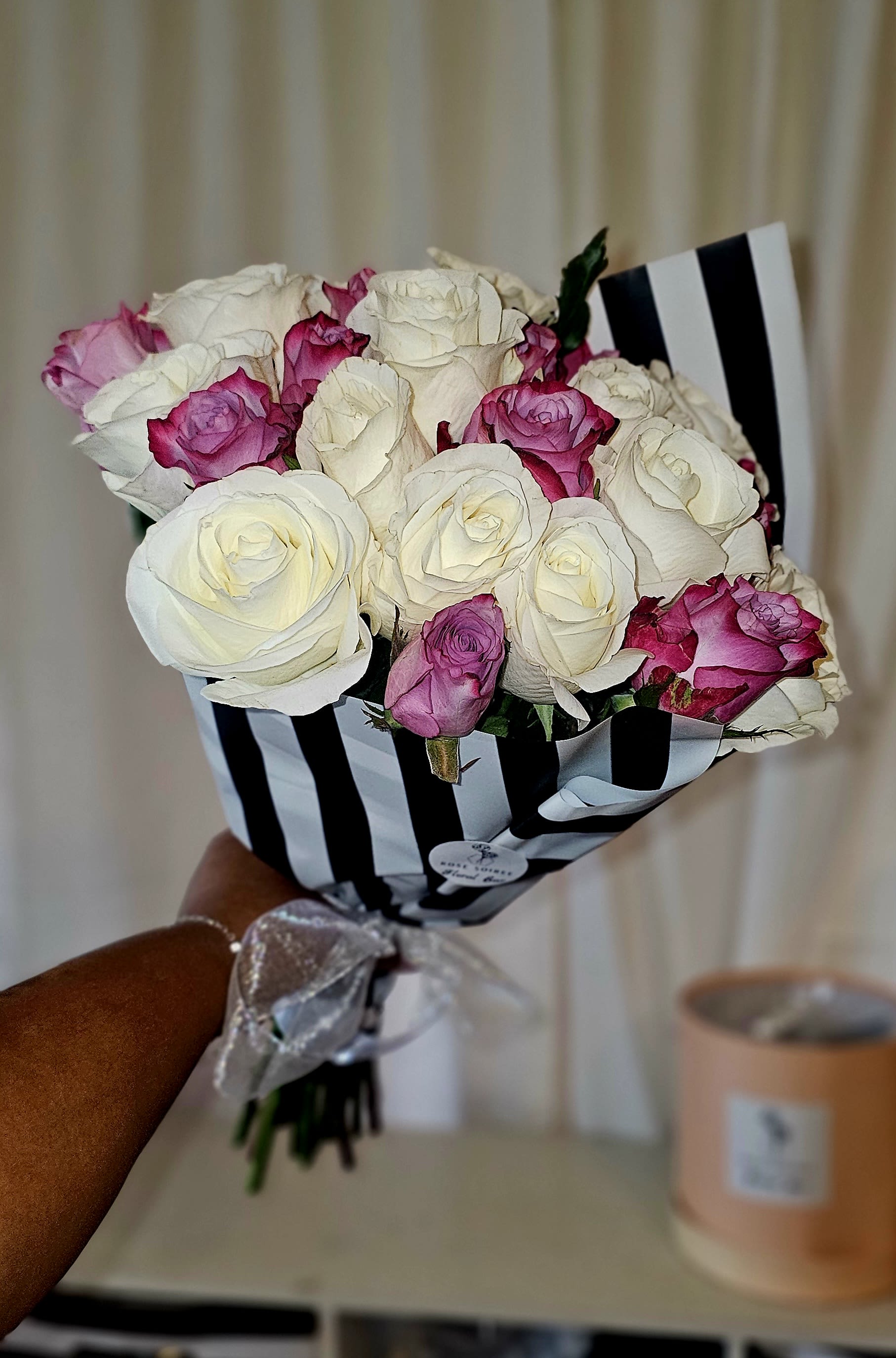 Bouquet of white and pink roses wrapped in black-and-white striped paper