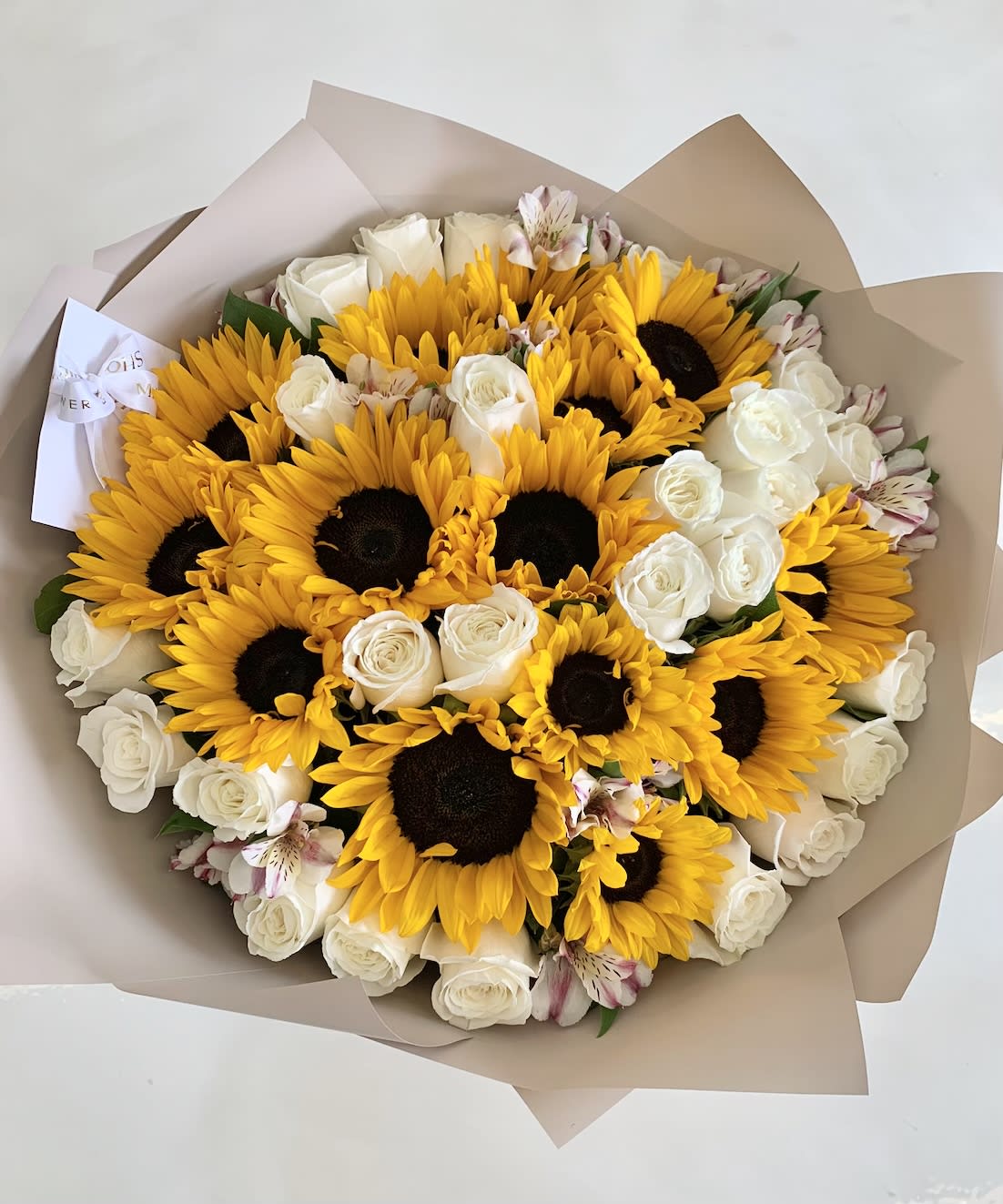 Bouquet of sunflowers, white roses, and pale pink alstroemeria in tan wrap