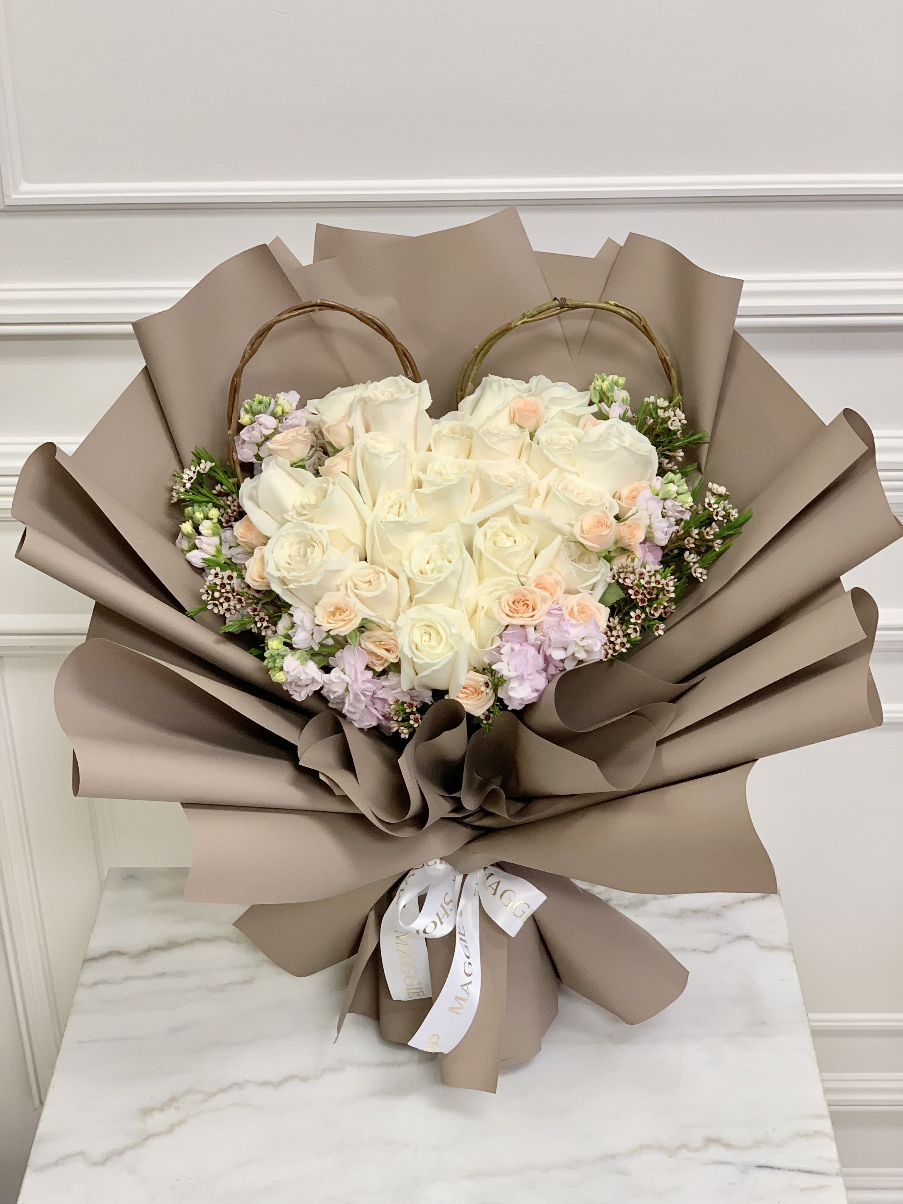 Heart-shaped bouquet of white and blush roses wrapped in taupe paper