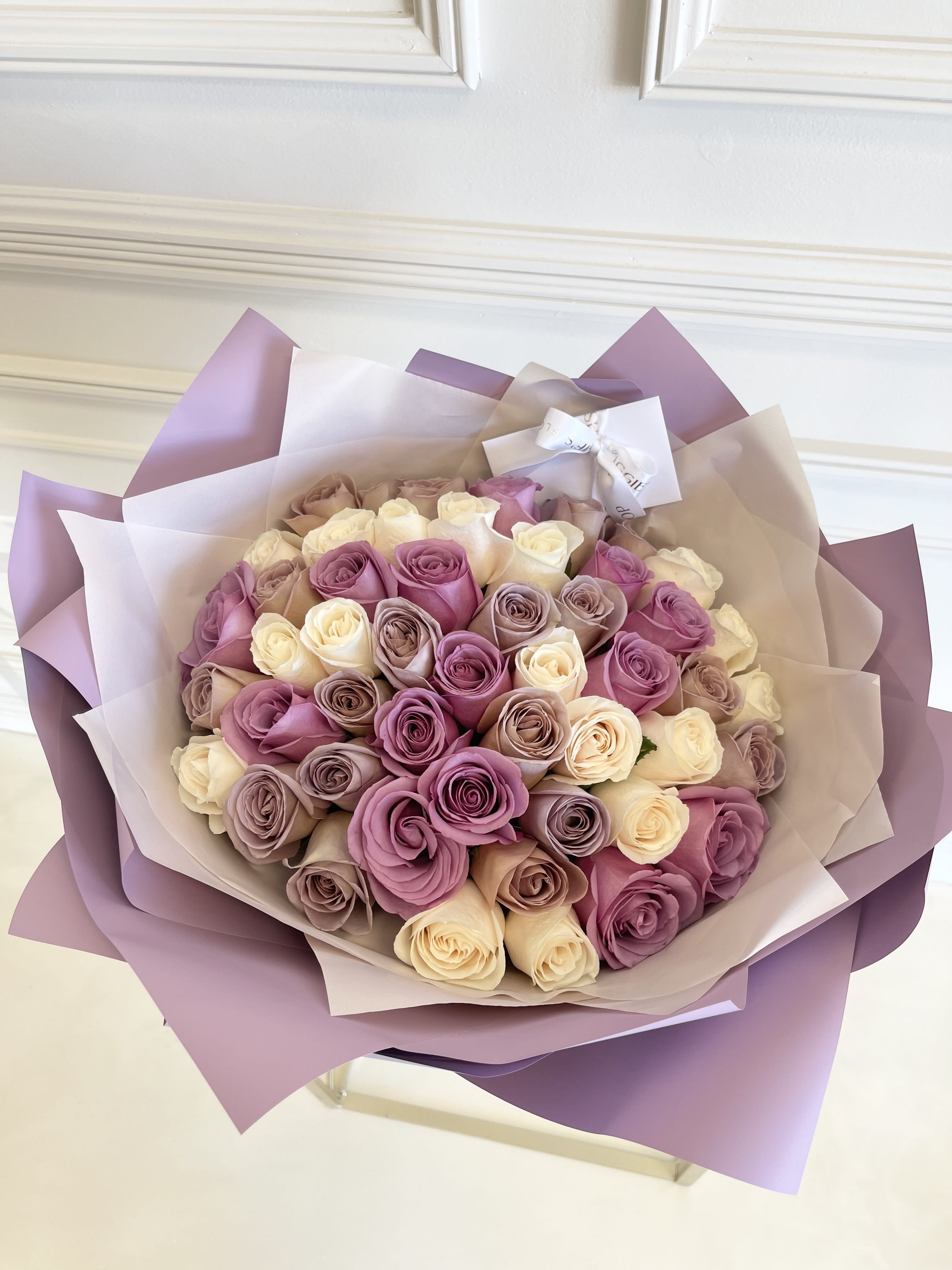Bouquet of pink, lavender, and cream roses wrapped in purple paper