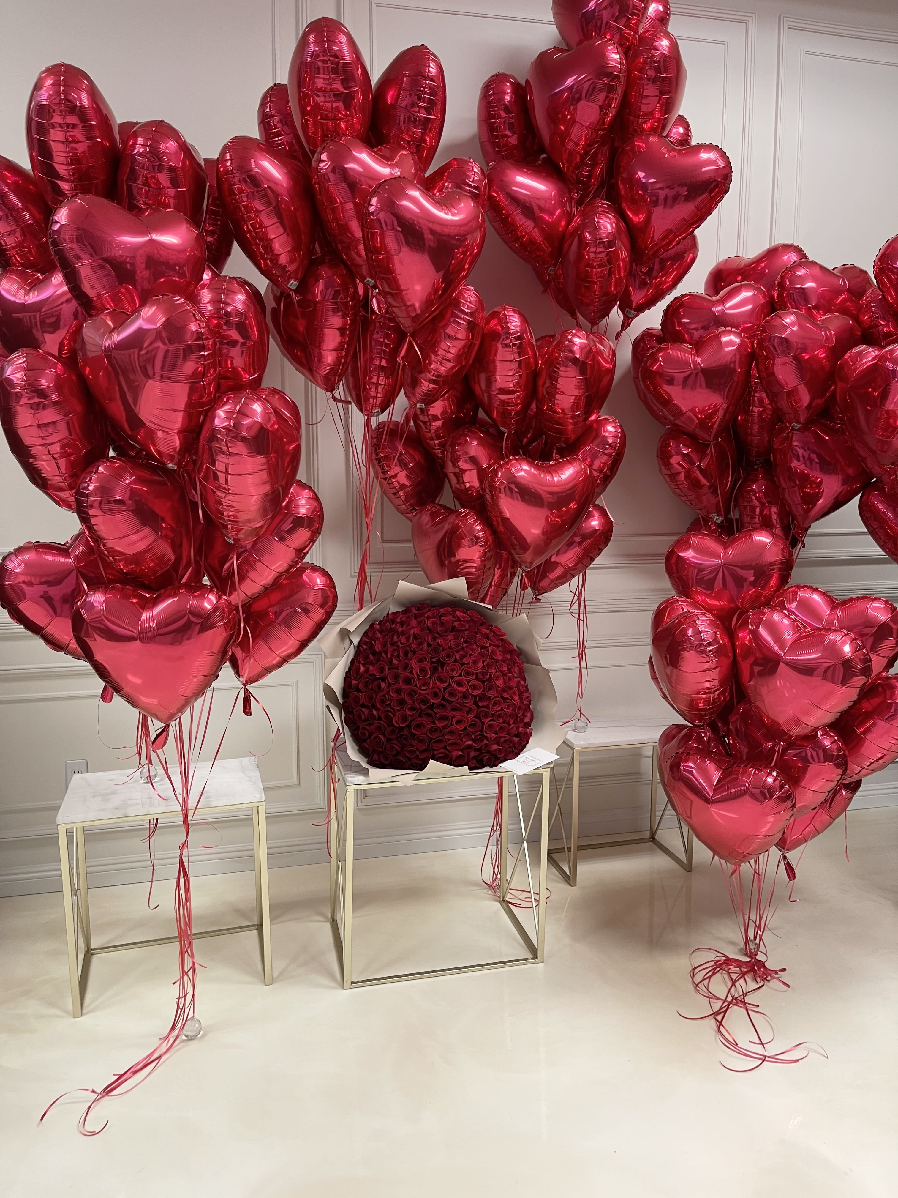 Clusters of red heart-shaped balloons surround a round bouquet of red roses.