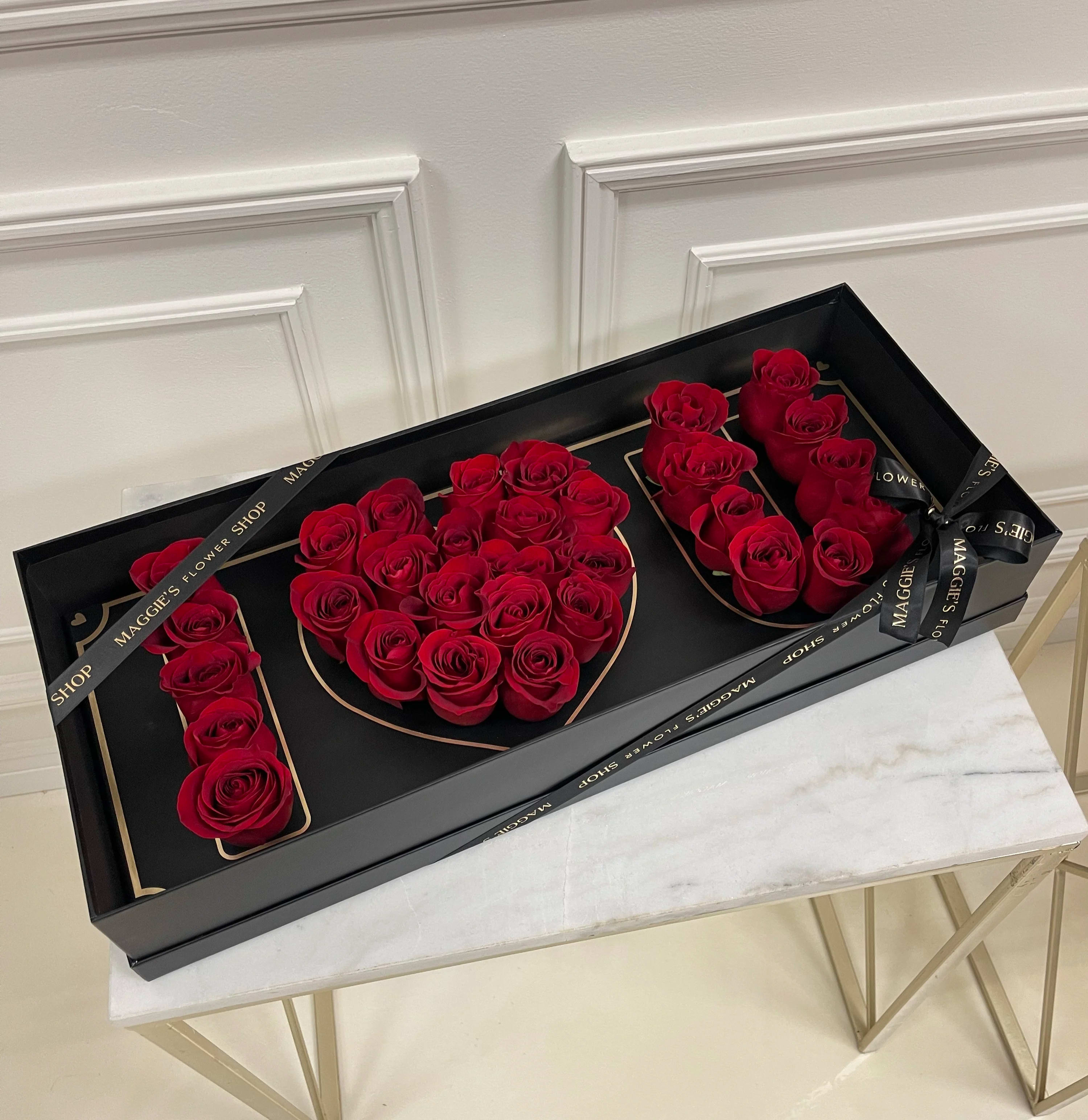 Red roses arranged in a black gift box spelling "LOVE"