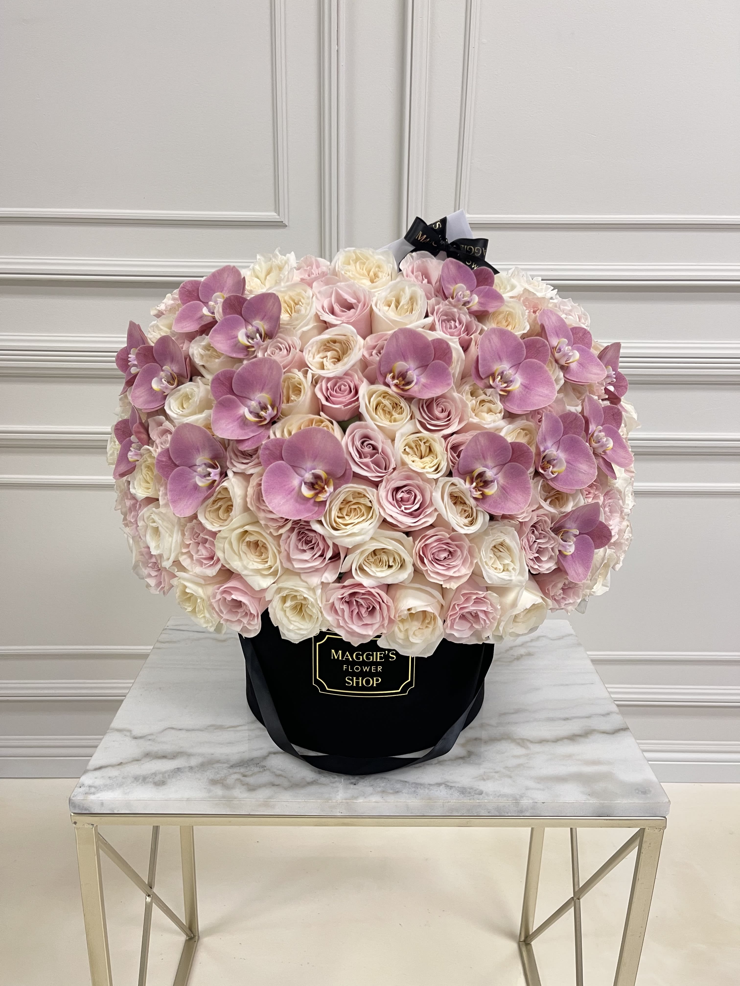 Large bouquet of pink and white roses with purple orchids in a black hat box