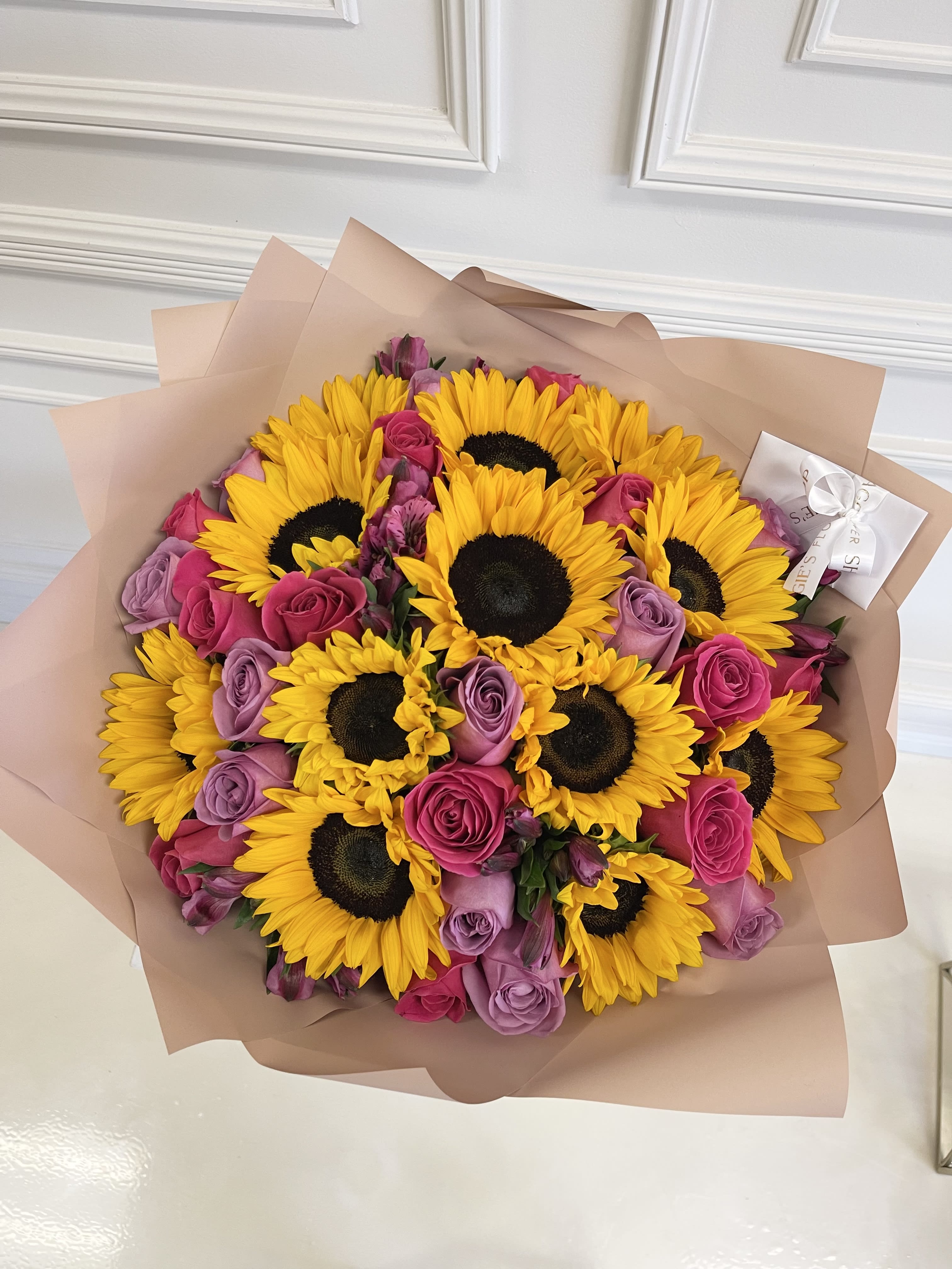Bouquet of yellow sunflowers and pink-purple roses wrapped in blush paper