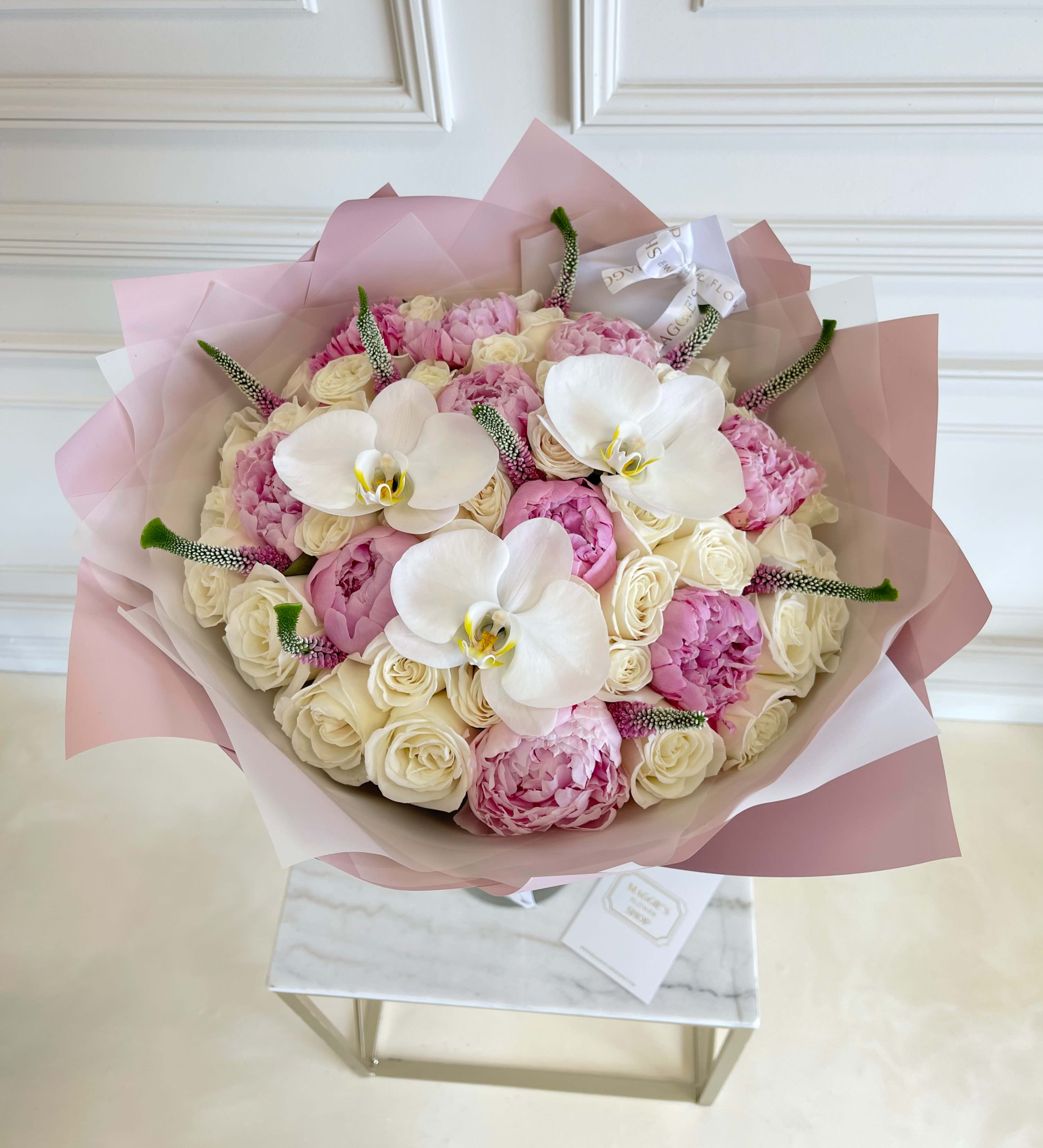 Bouquet of pink and cream flowers with white orchids wrapped in blush paper
