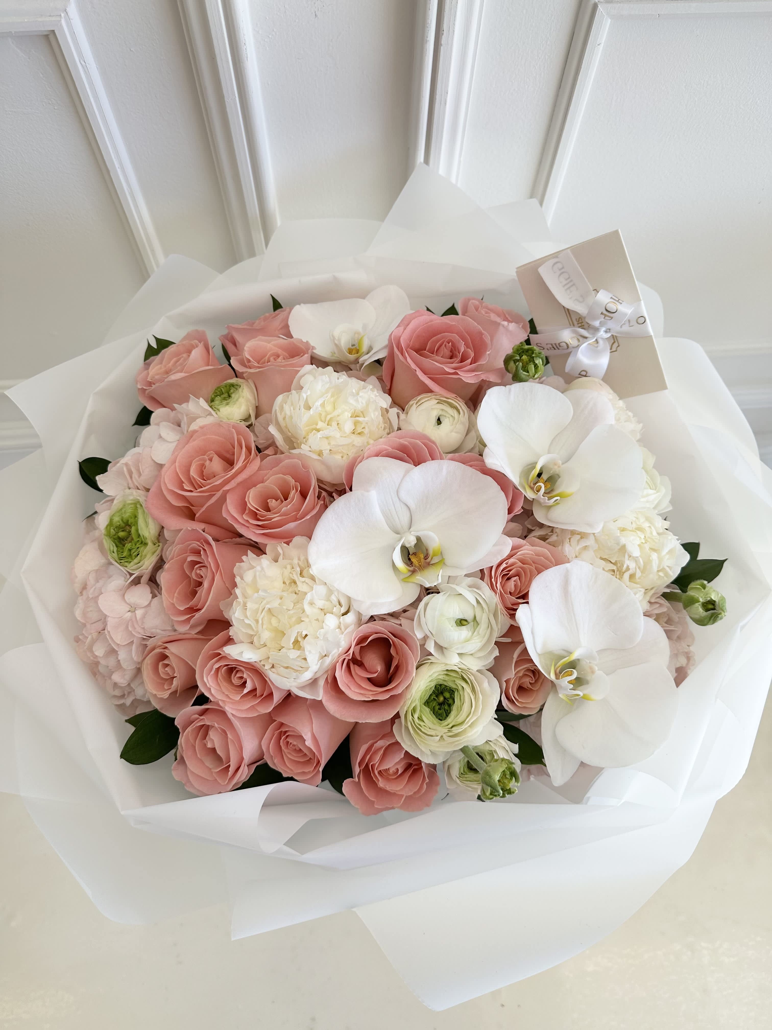 Pink rose bouquet with white orchids and cream blooms wrapped in white paper