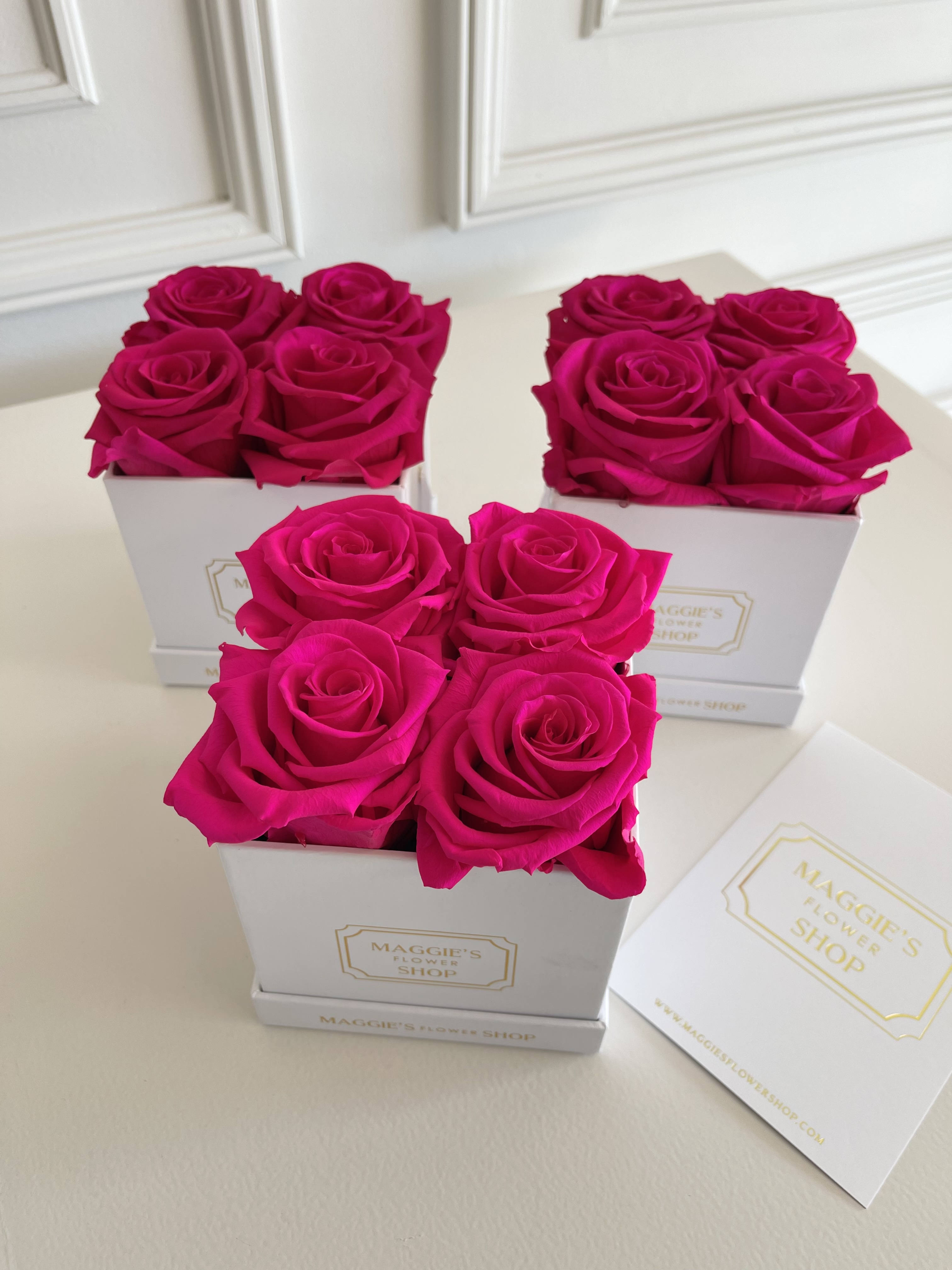 Three white boxes of hot pink roses on a table