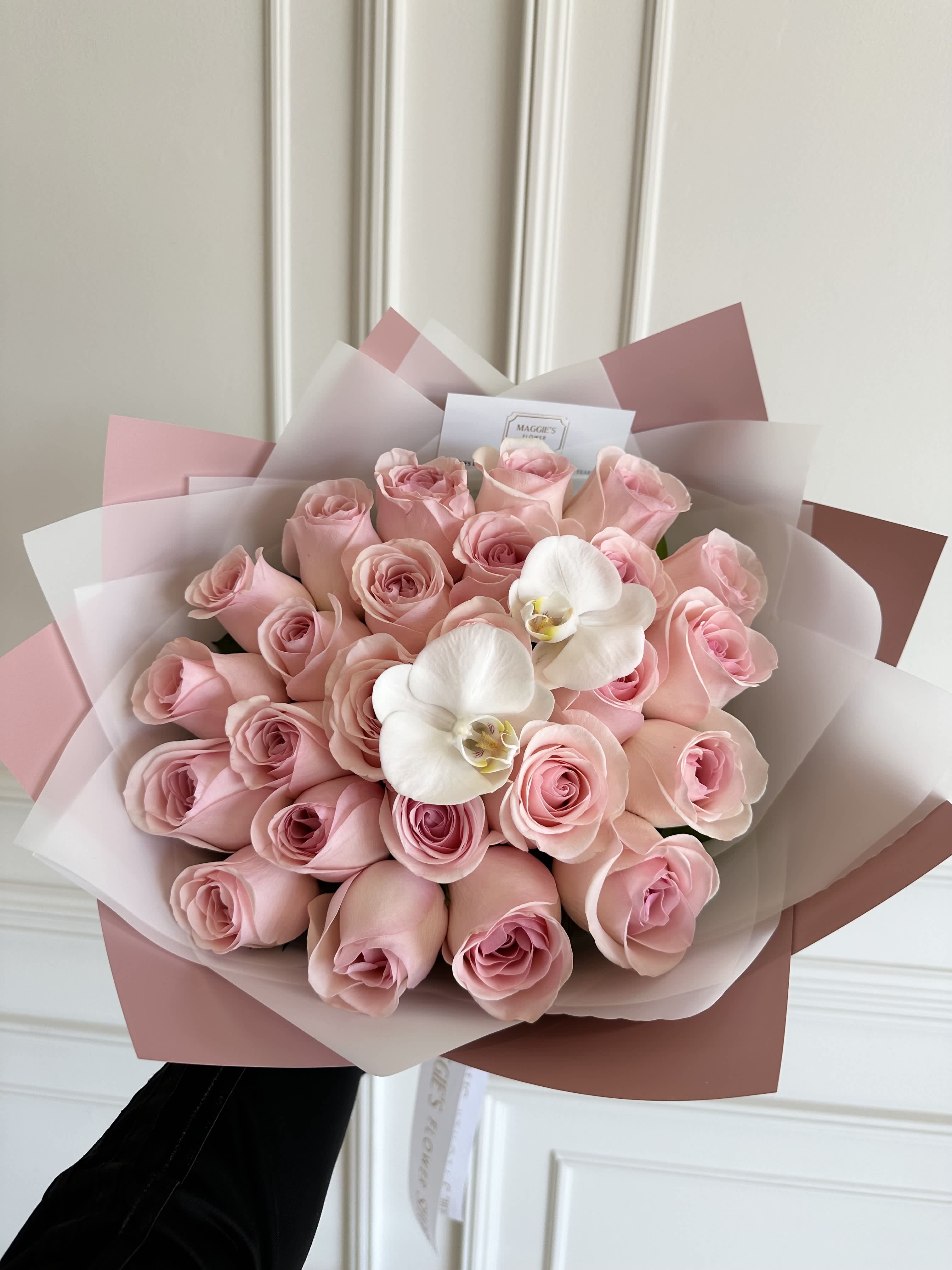 Bouquet of pink roses with two white orchids wrapped in pink paper