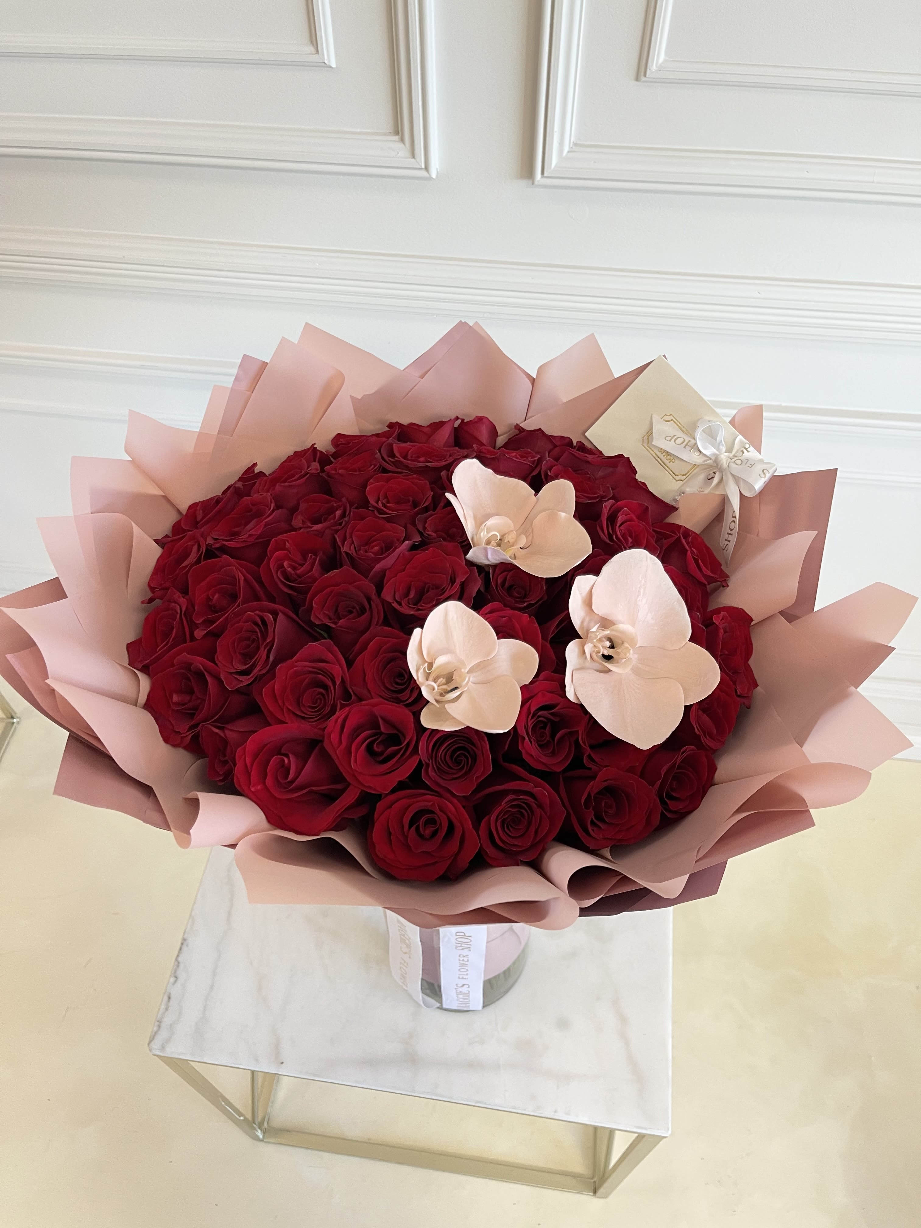 Bouquet of red roses with pale pink orchid accents in pink wrap
