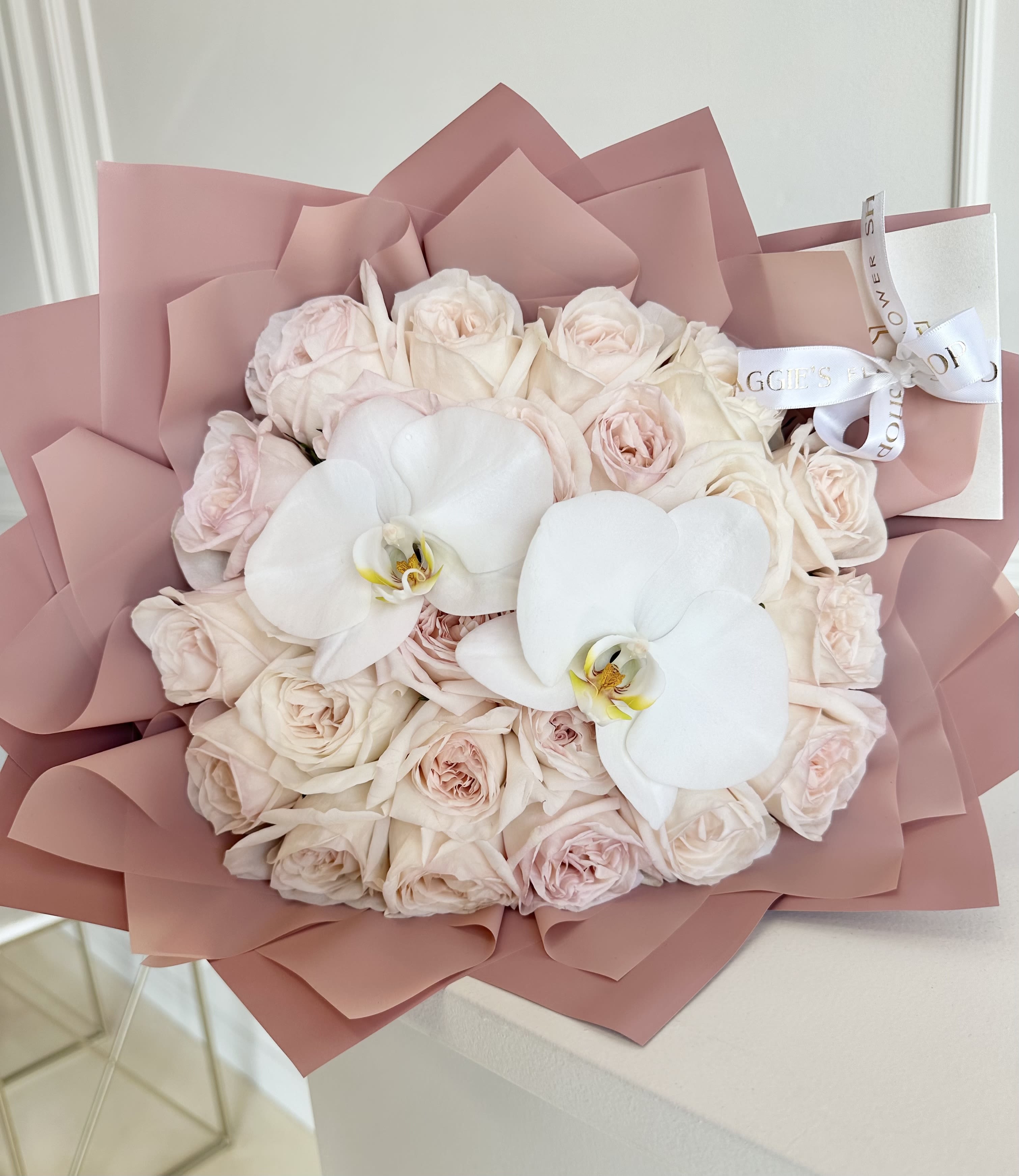 Bouquet of pale pink roses with two white orchids in pink wrapping