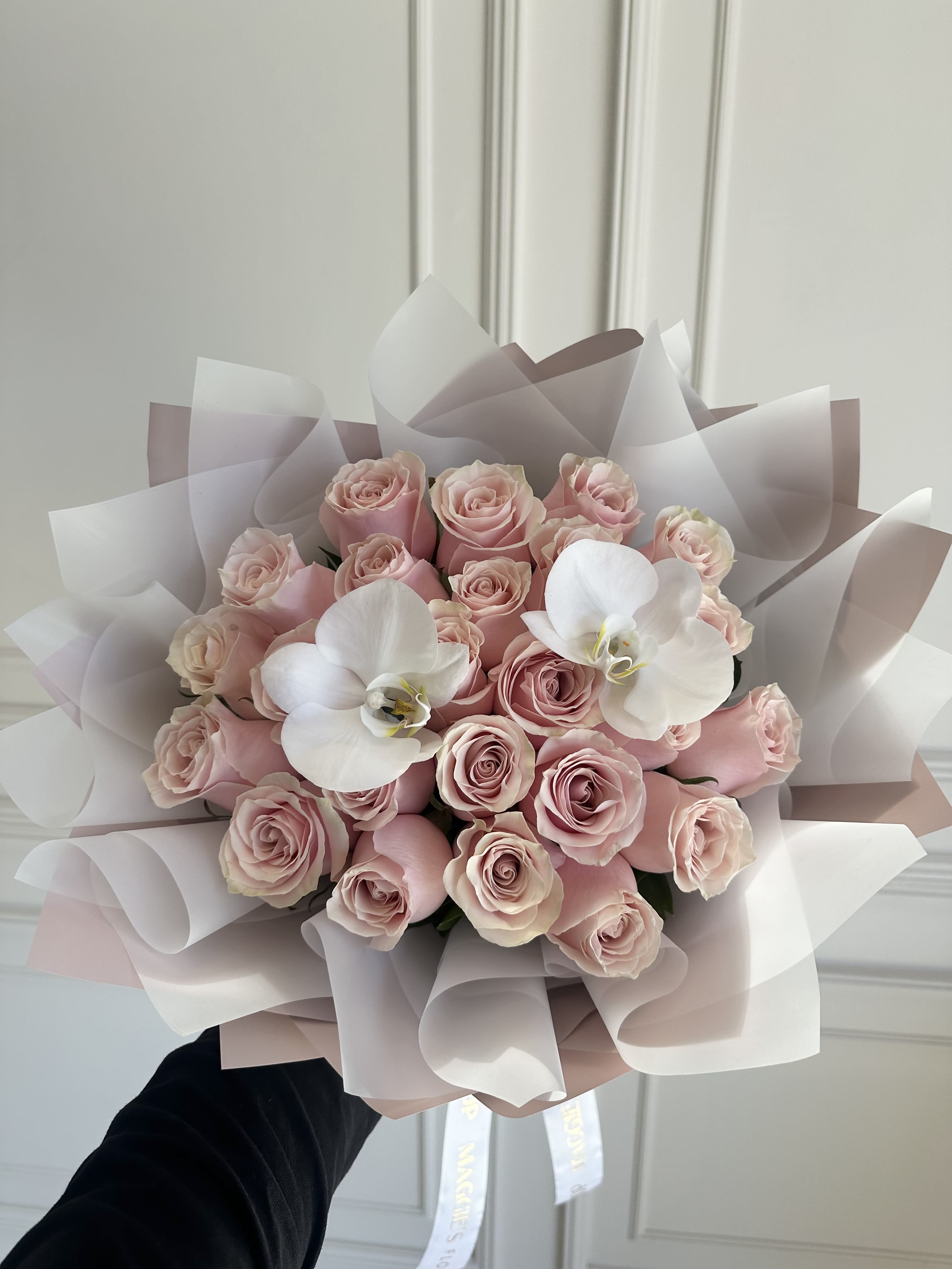 Bouquet of pale pink roses with two white orchids wrapped in blush paper