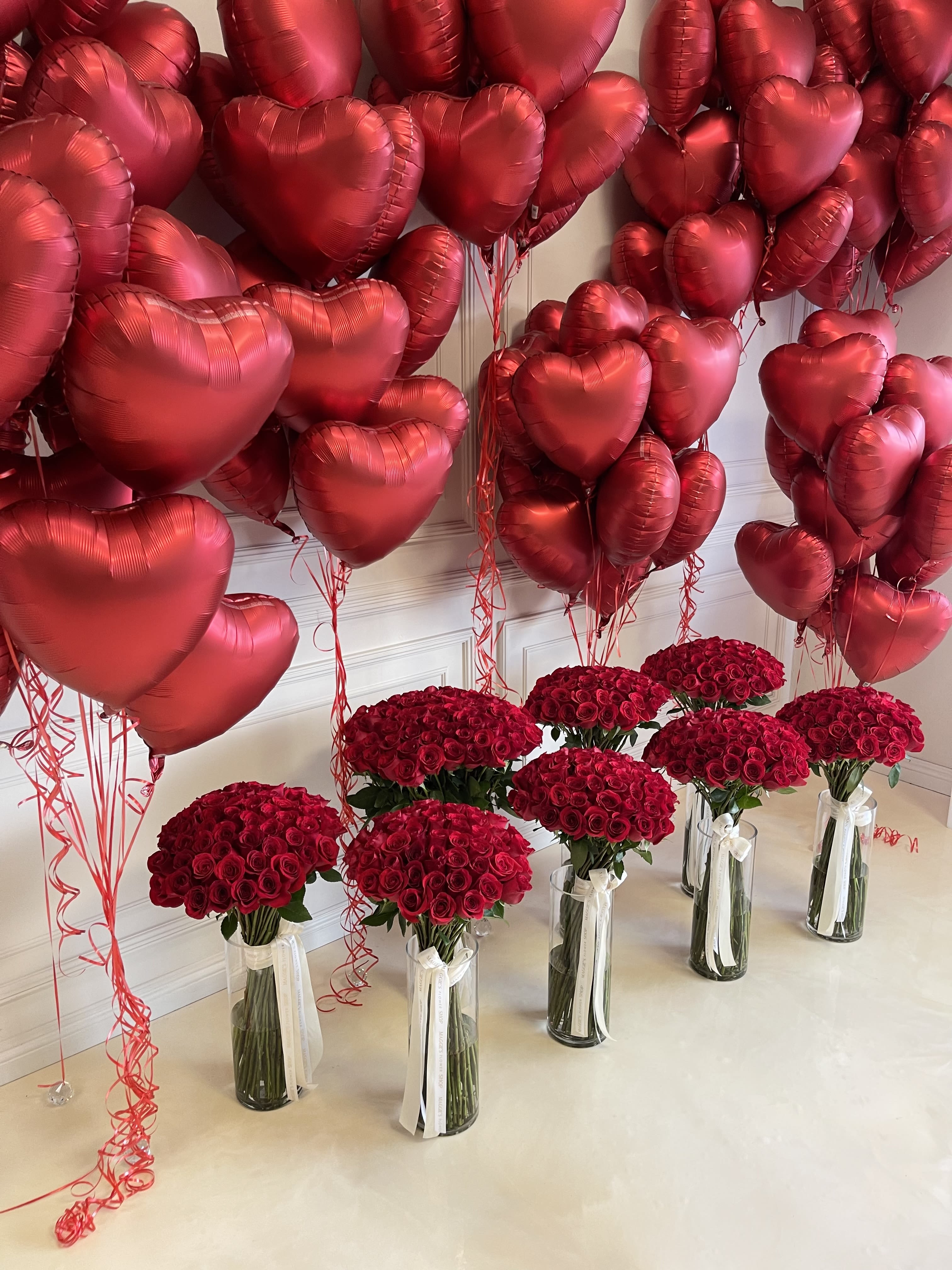 Red heart balloons above bouquets of red roses in glass vases