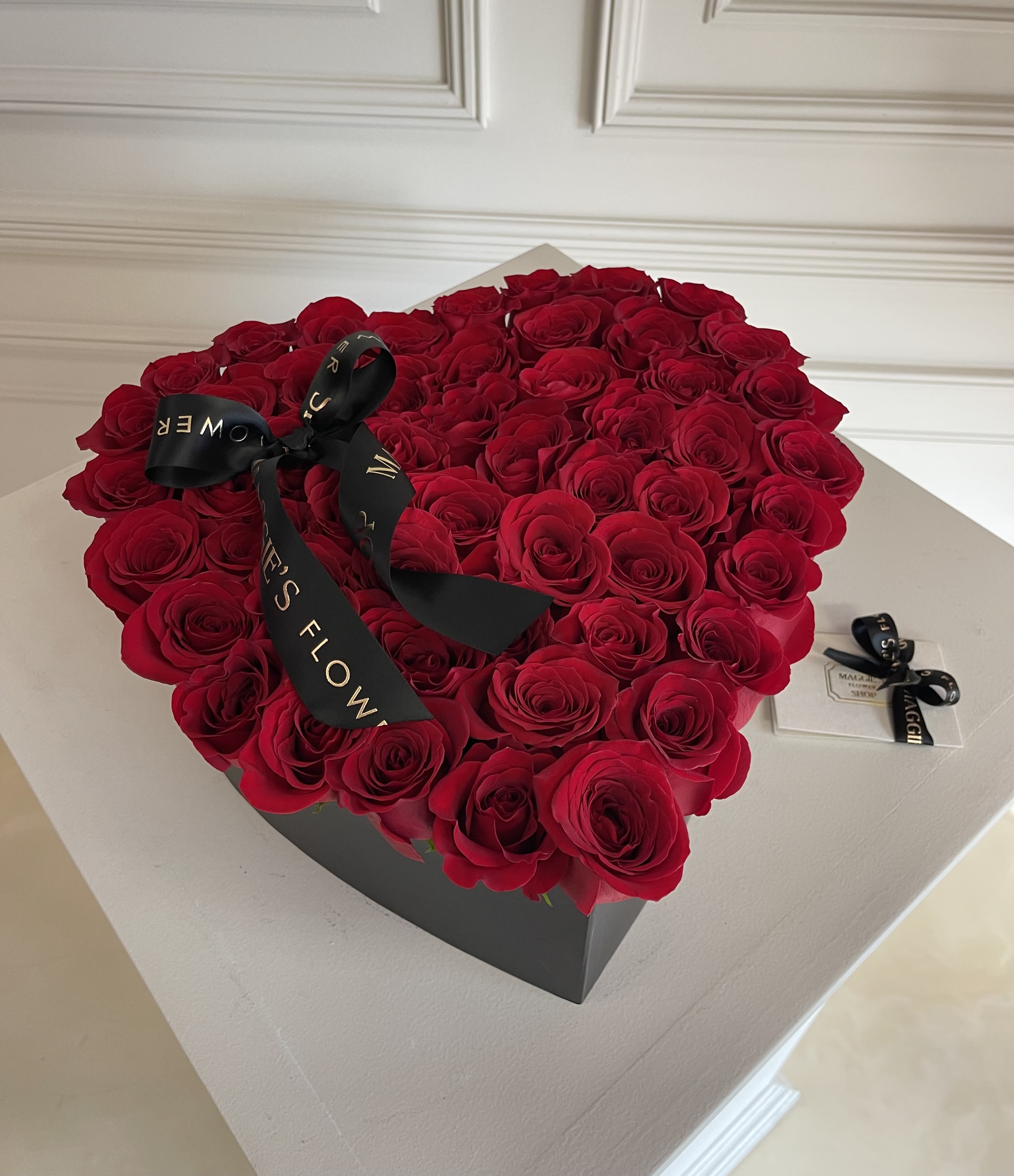 Heart-shaped box filled with red roses and a black ribbon