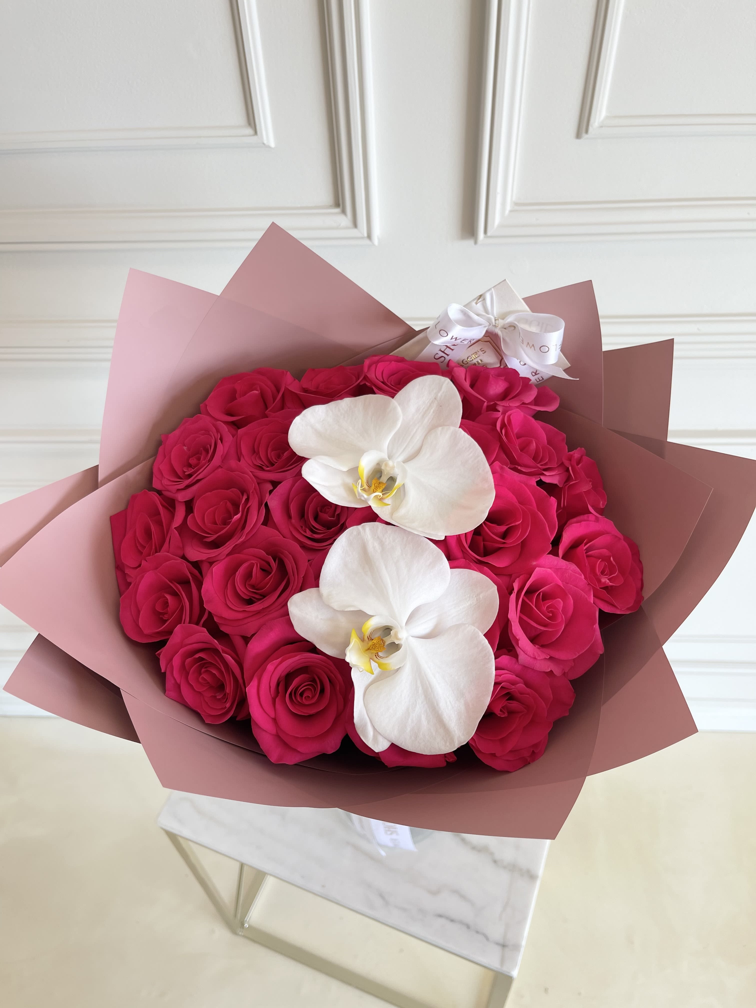 Bouquet of hot pink roses with two white orchids in pink wrapping