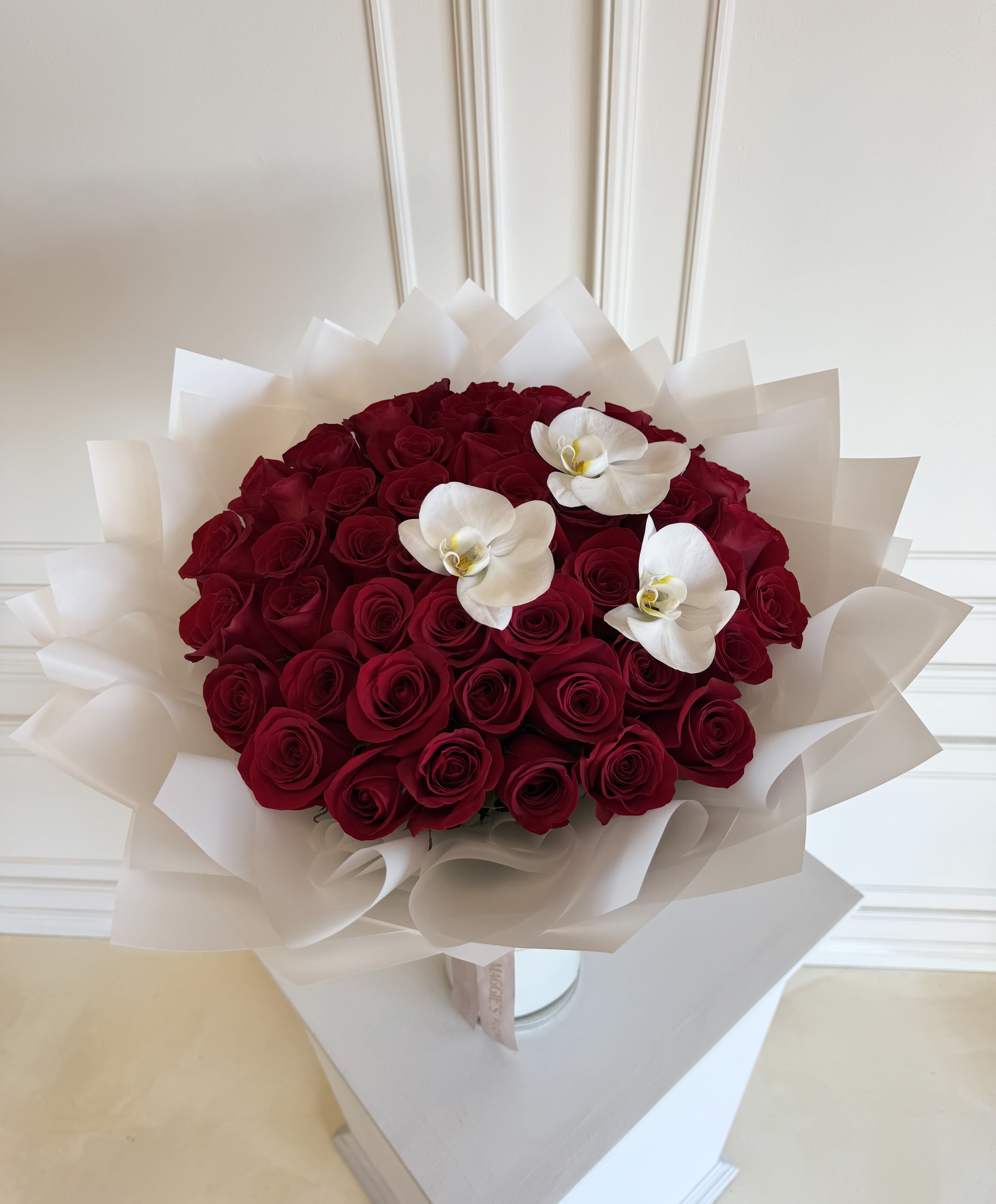 Bouquet of red roses with three white orchids wrapped in white paper