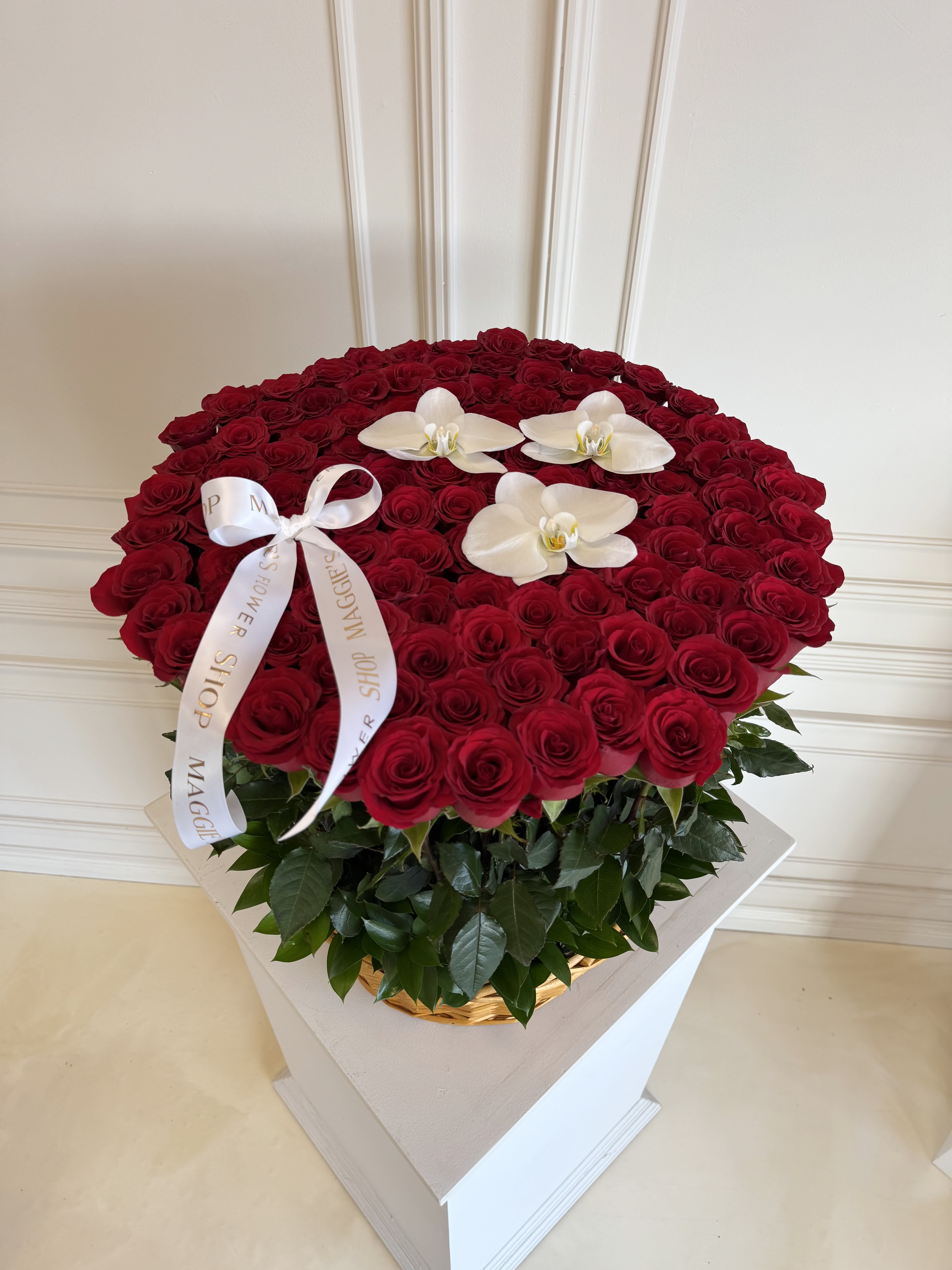 Large round arrangement of red roses with white orchids and a ribbon