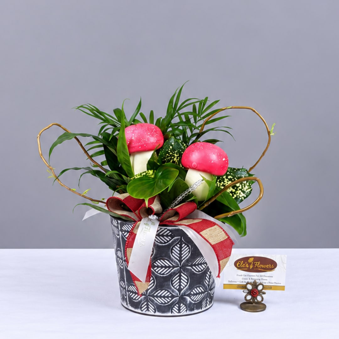 Potted arrangement with pink mushroom ornaments and green foliage in a patterned container