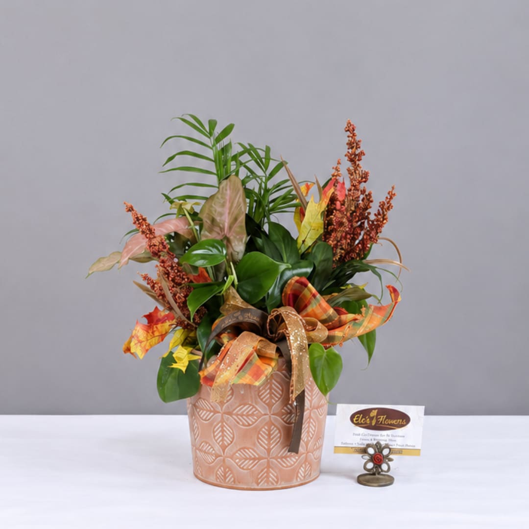 Autumn arrangement in a patterned ceramic pot with ribbon and mixed foliage
