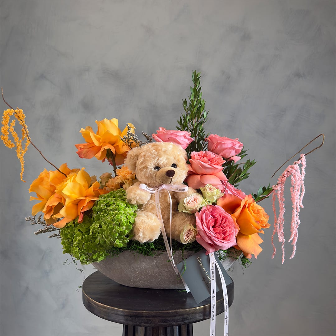 Teddy bear in a flower arrangement with pink and orange roses in a gray bowl