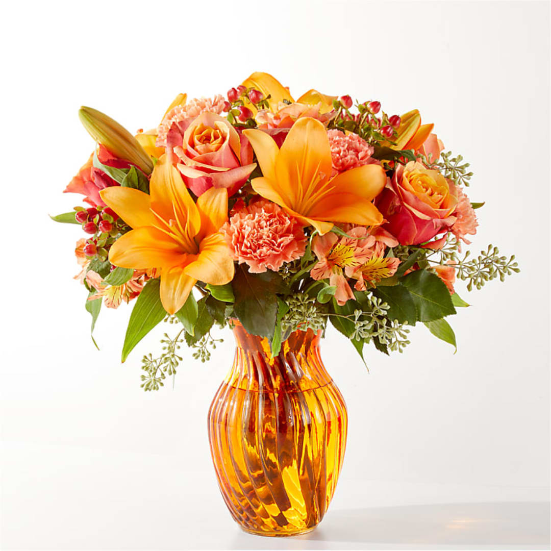 Orange lilies and roses arranged in an amber glass vase