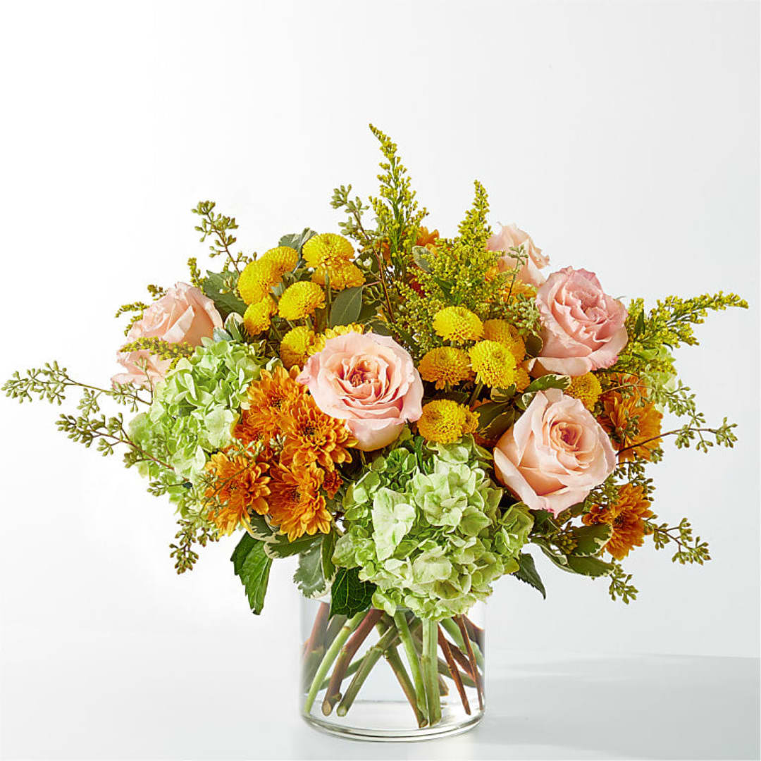 Bouquet of pink roses, green hydrangeas, and yellow-orange mums in a clear glass vase