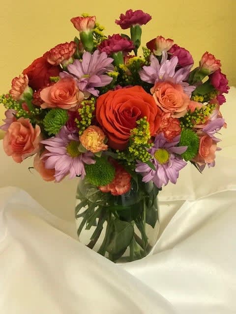 Mixed bouquet of roses, carnations, and purple daisies in a glass vase