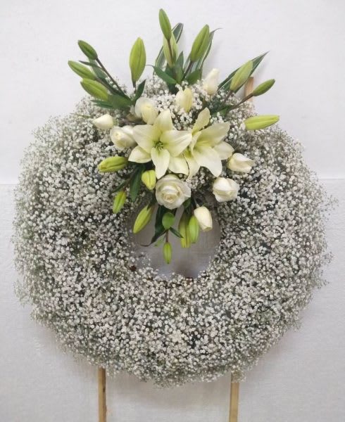 Large white wreath of baby's breath with white lilies and roses on a stand