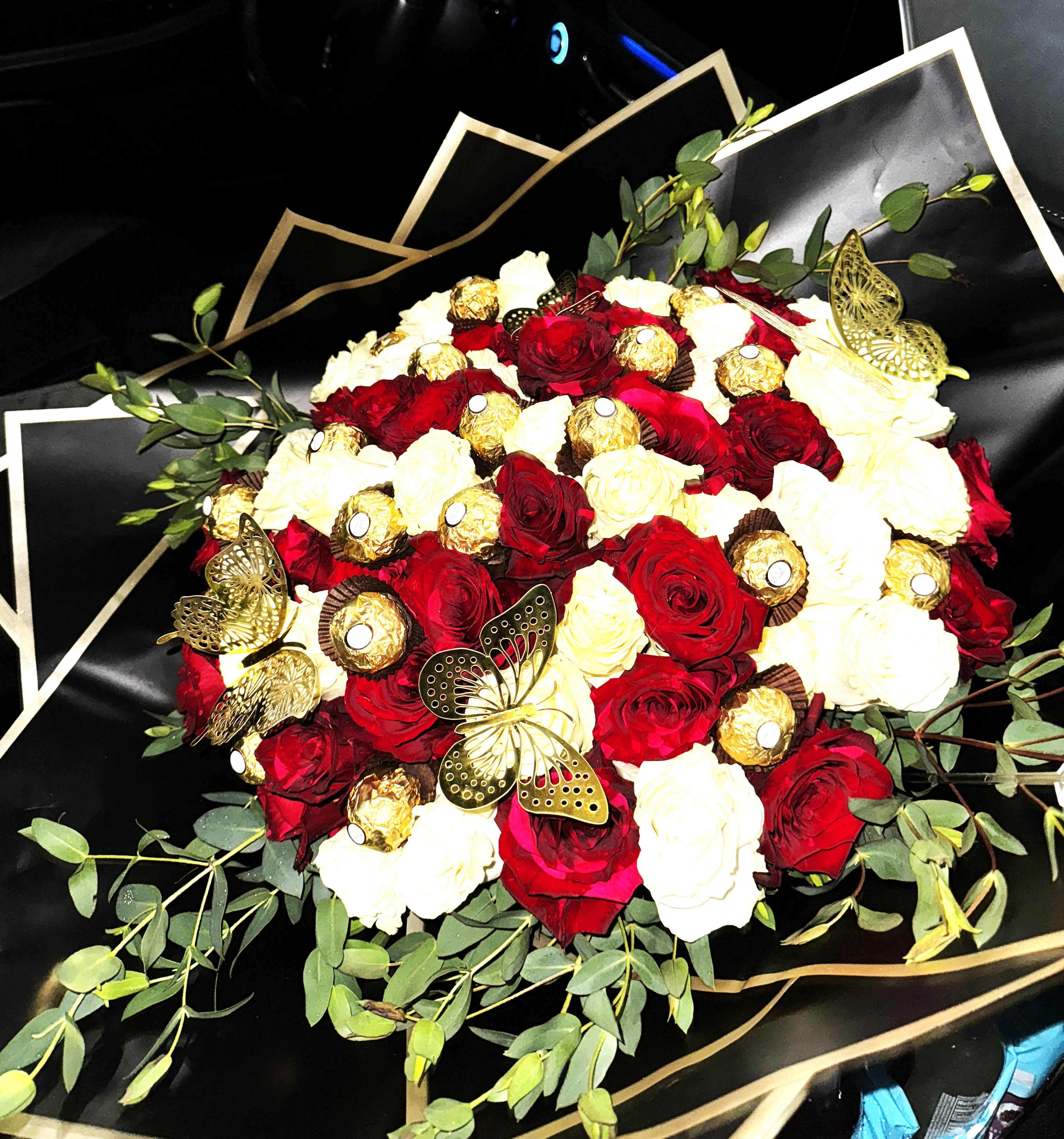 Round bouquet of red and white roses with gold-wrapped chocolates and gold butterflies in black wrapping