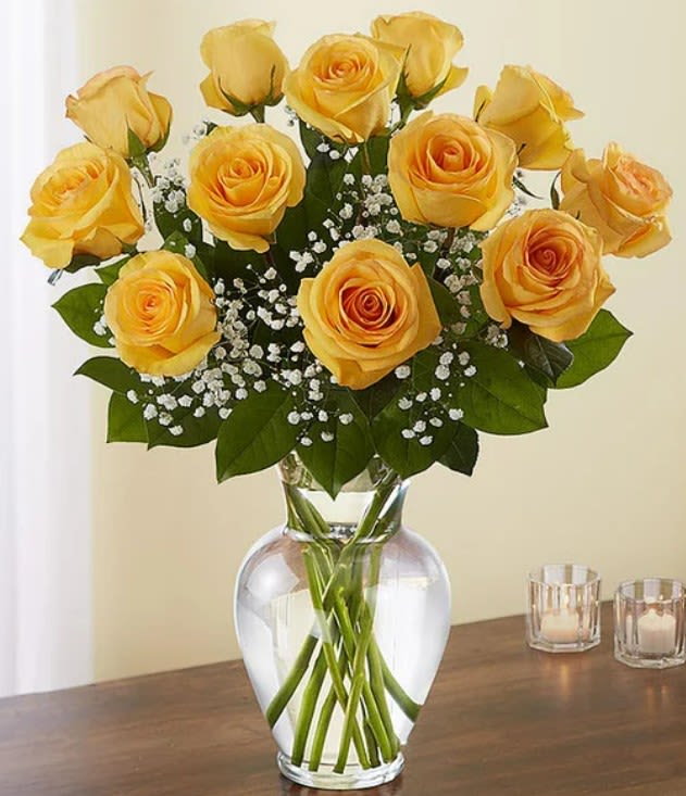 Dozen yellow roses with white filler flowers arranged in a clear glass vase