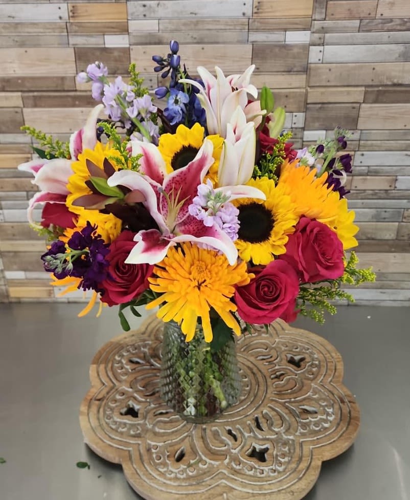 Mixed bouquet with lilies, sunflowers, and roses in a glass vase