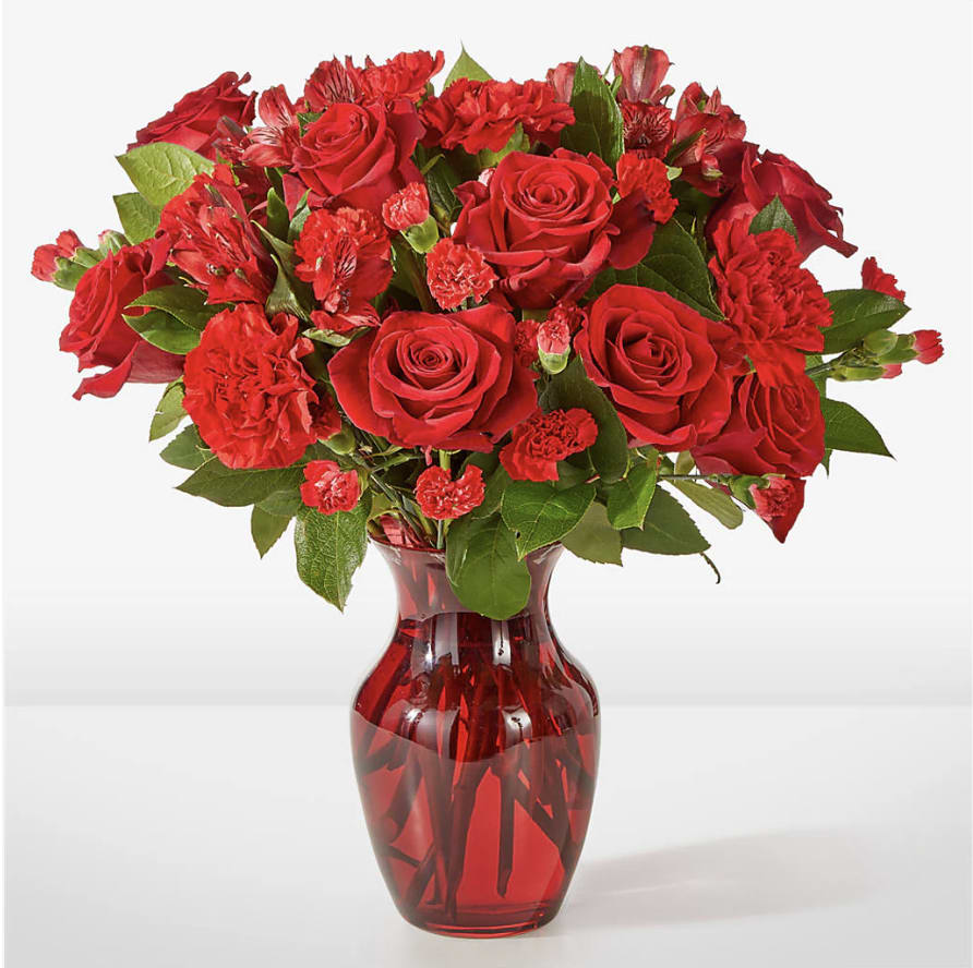 Red roses and carnations arranged in a red glass vase