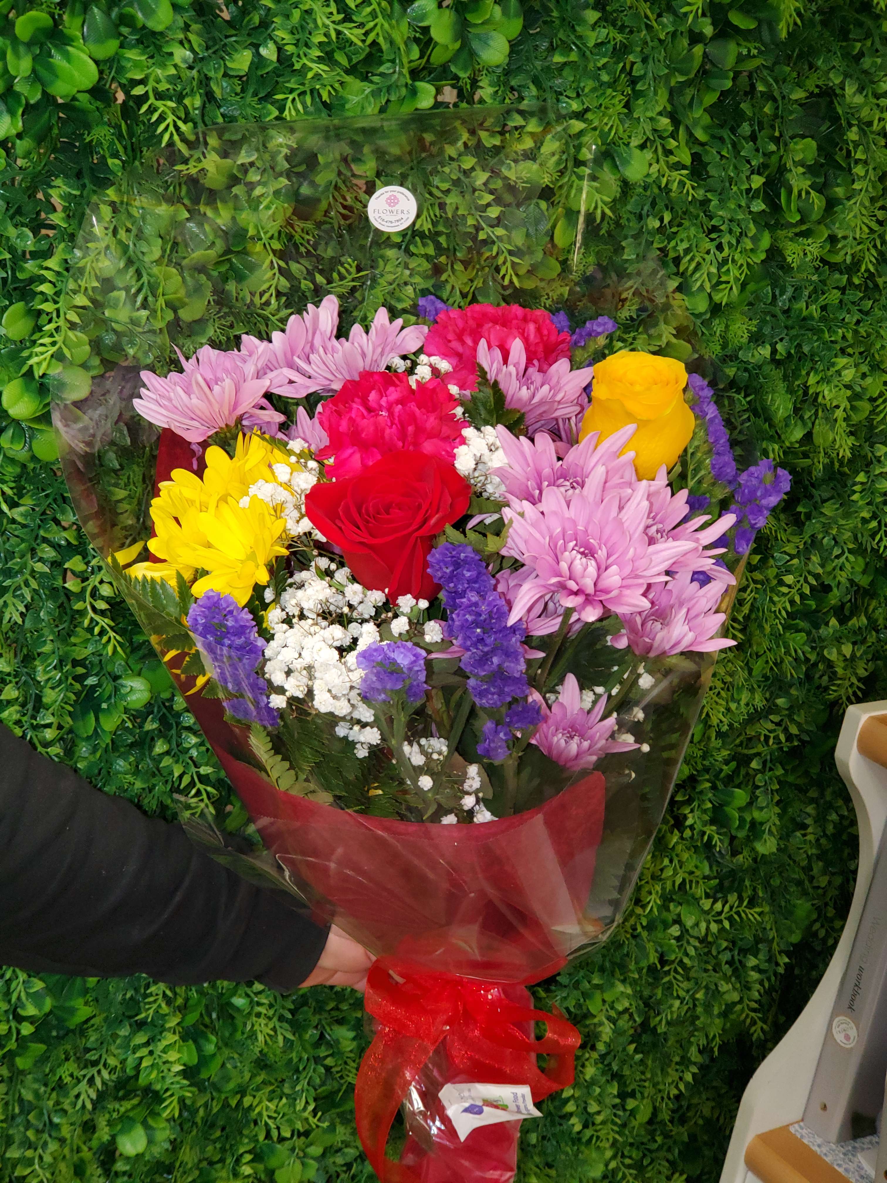 Mixed bouquet of roses and chrysanthemums wrapped in red cellophane with a bow